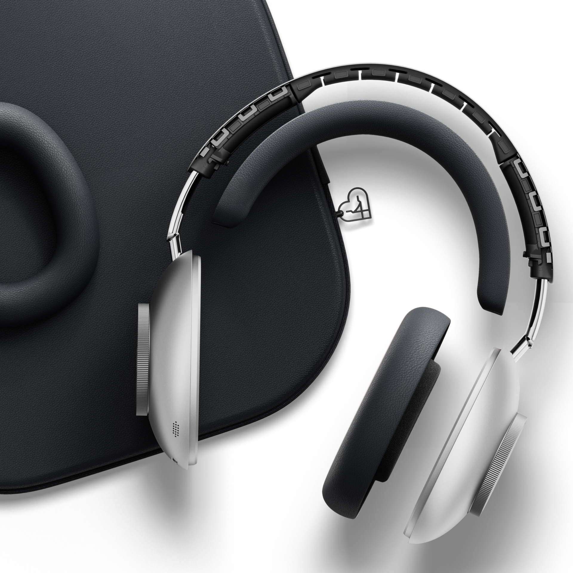 Over-Ear-Kopfhörer mit silbernen Akzenten und schwarzen Ohrmuscheln, die auf einer strukturierten schwarzen Oberfläche liegen. Ein herzförmiger Anhänger ist sichtbar.
