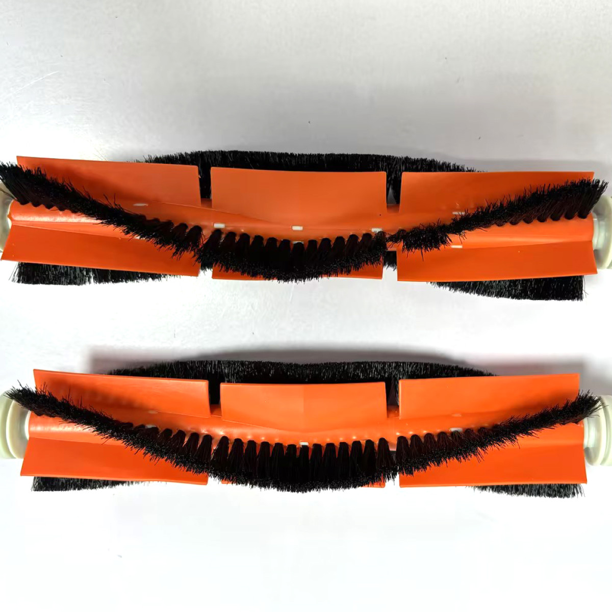 Dwie pomarańczowo-czarne rolki szczotki do odkurzacza leżą na białej powierzchni. Szczotki są czarne, a podstawa pomarańczowa.