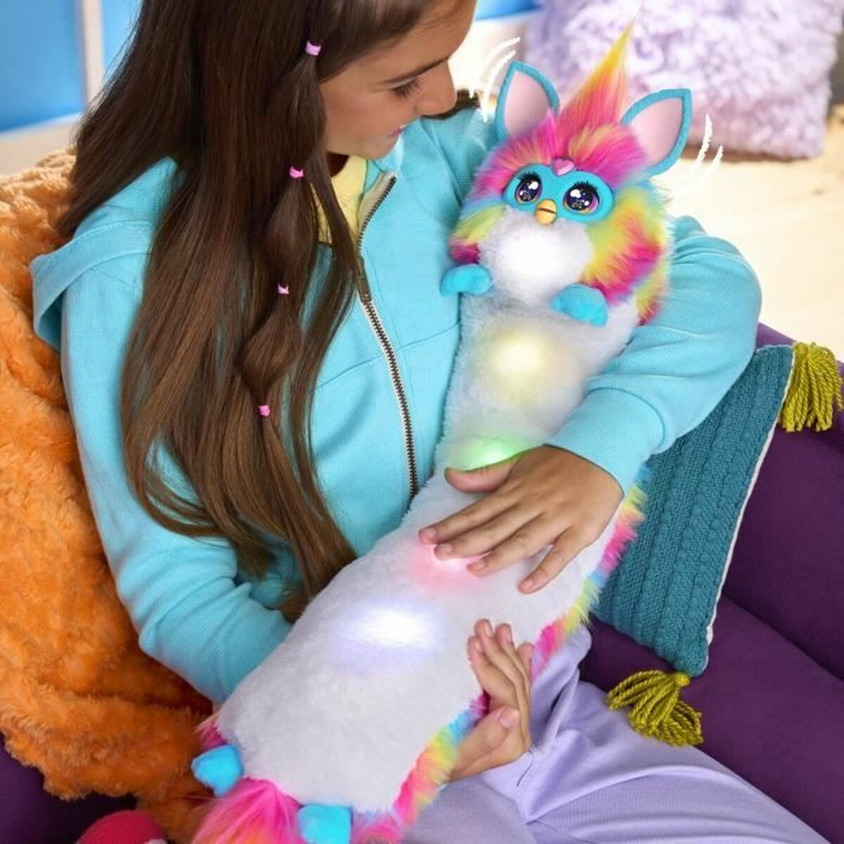 Une fille serre dans ses bras un jouet coloré semblable à Furby avec des lumières vives. Le jouet est long et a des poils arc-en-ciel. La fille porte une veste bleue.