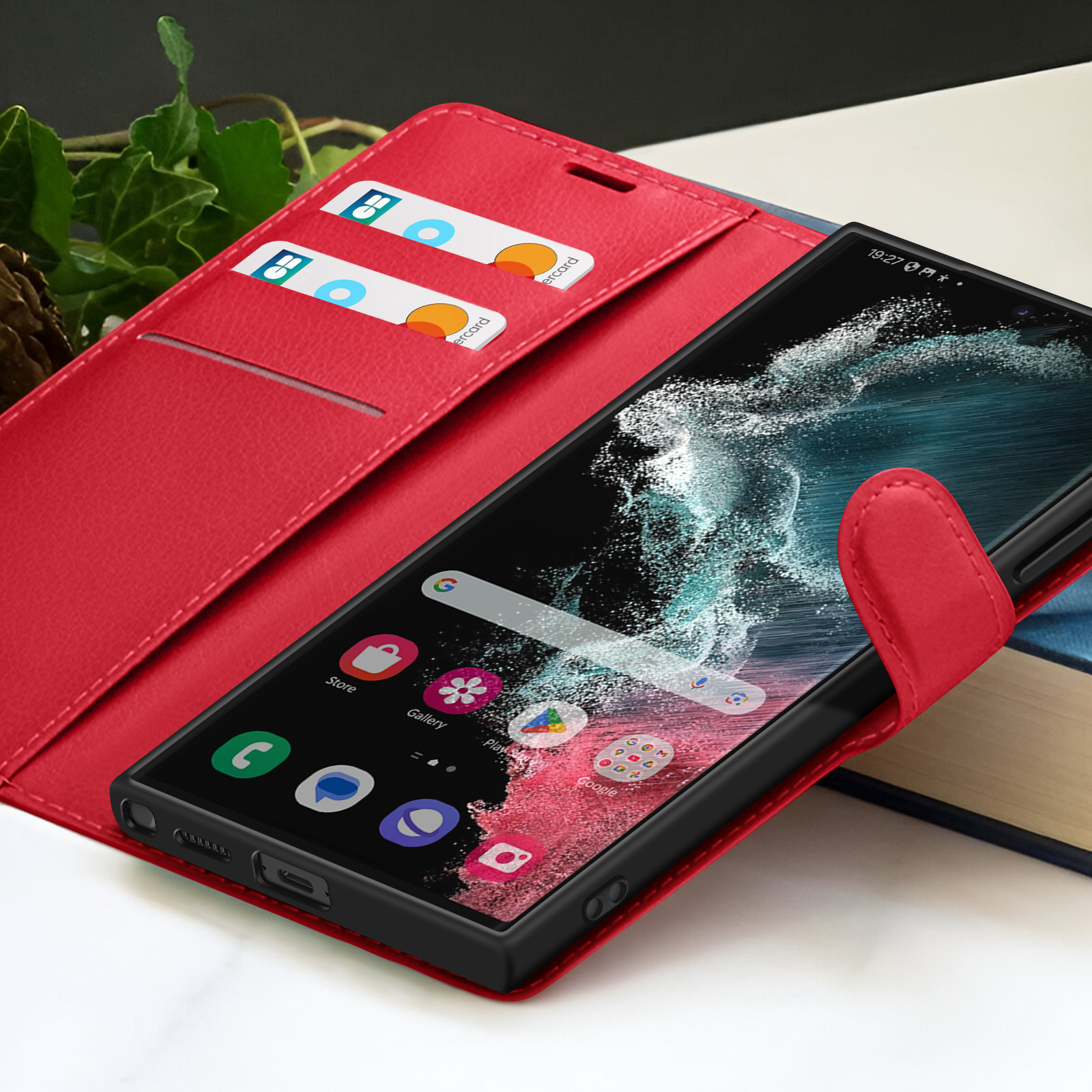 Étui de téléphone rouge avec un téléphone affichant des icônes d'applications. Cartes de crédit visibles dans l'étui. Livre en arrière-plan.