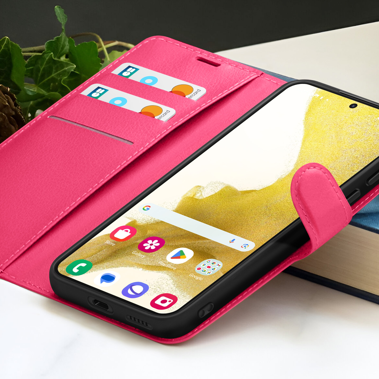Étui de téléphone rose avec un téléphone affichant des applications. Cartes de crédit dans l'étui. Le téléphone est sur une surface blanche et un livre.