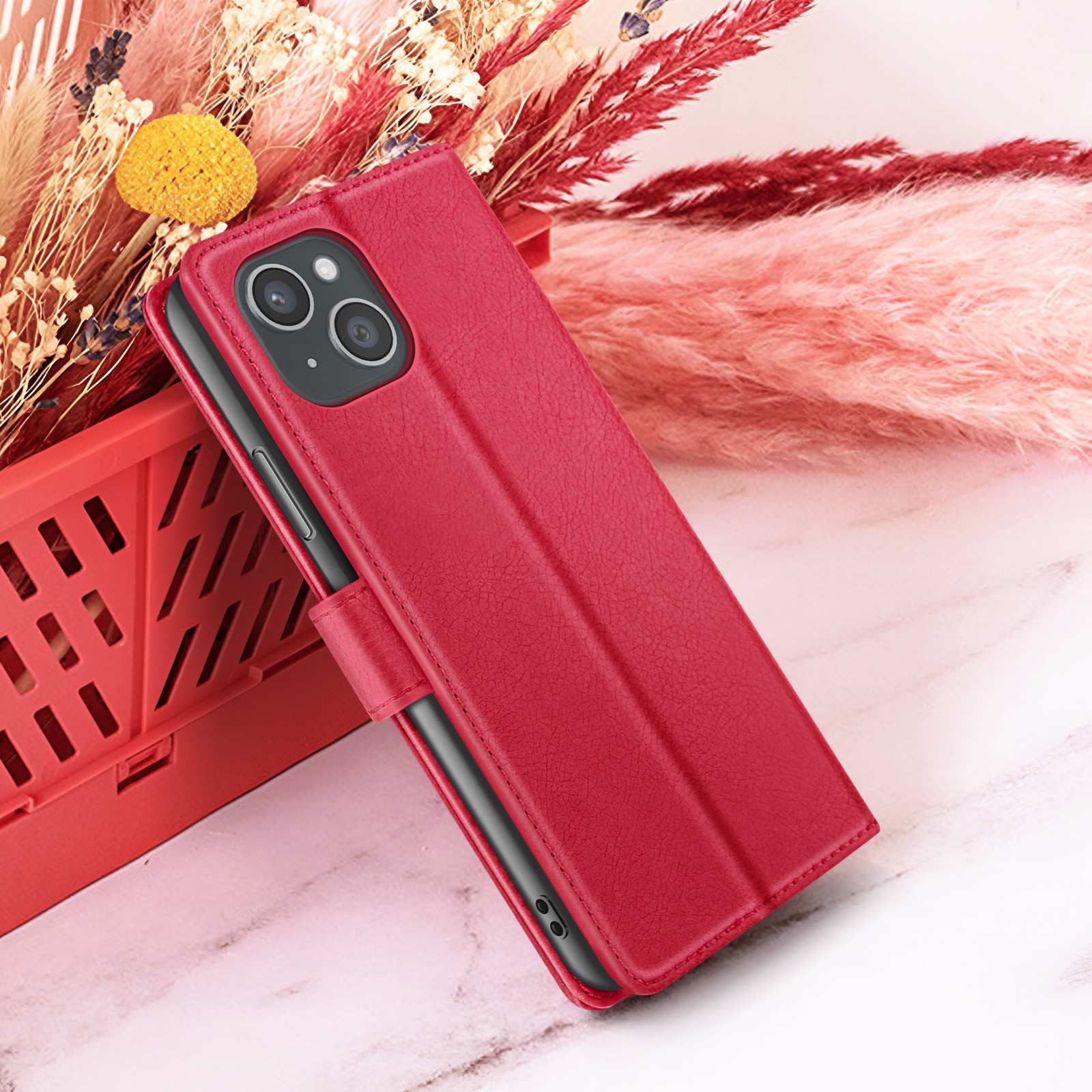 Een rode telefoonhoes met een telefoon erin, geplaatst in een rode container met bloemen op de achtergrond.