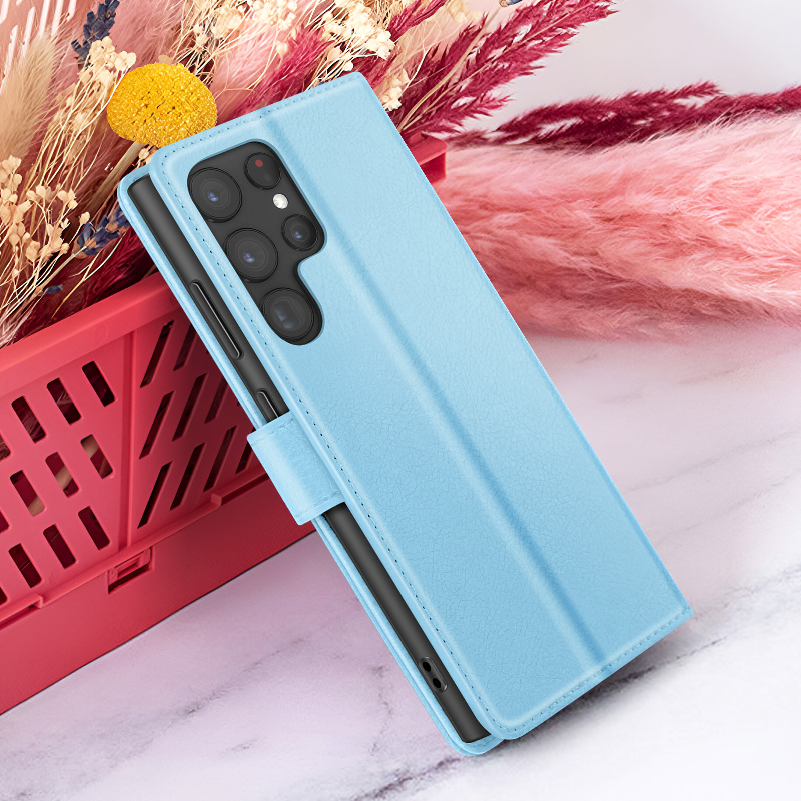 Un étui de téléphone bleu clair sur une surface en marbre. Des fleurs séchées dans un panier rouge en arrière-plan.