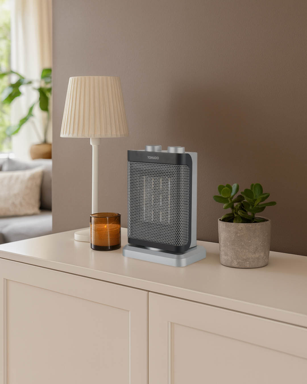 Een kleine kachel, lamp, kaars en potplant staan op een kast. Een bank en een muur staan op de achtergrond.