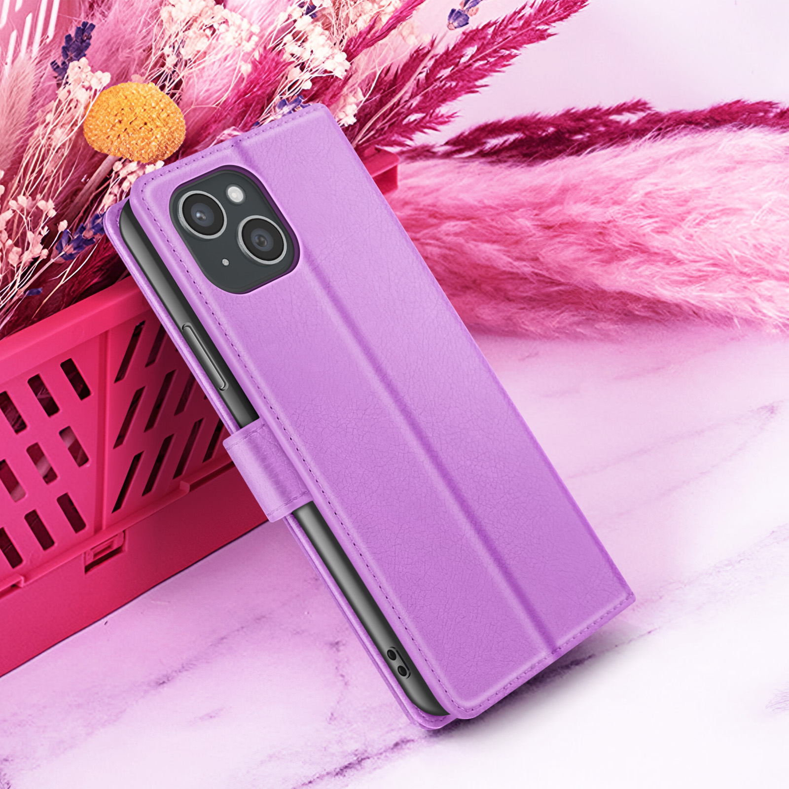 Een paarse telefoonhoes is open en toont een telefoon. Roze bloemen en een doos op de achtergrond. Het oppervlak is marmer.
