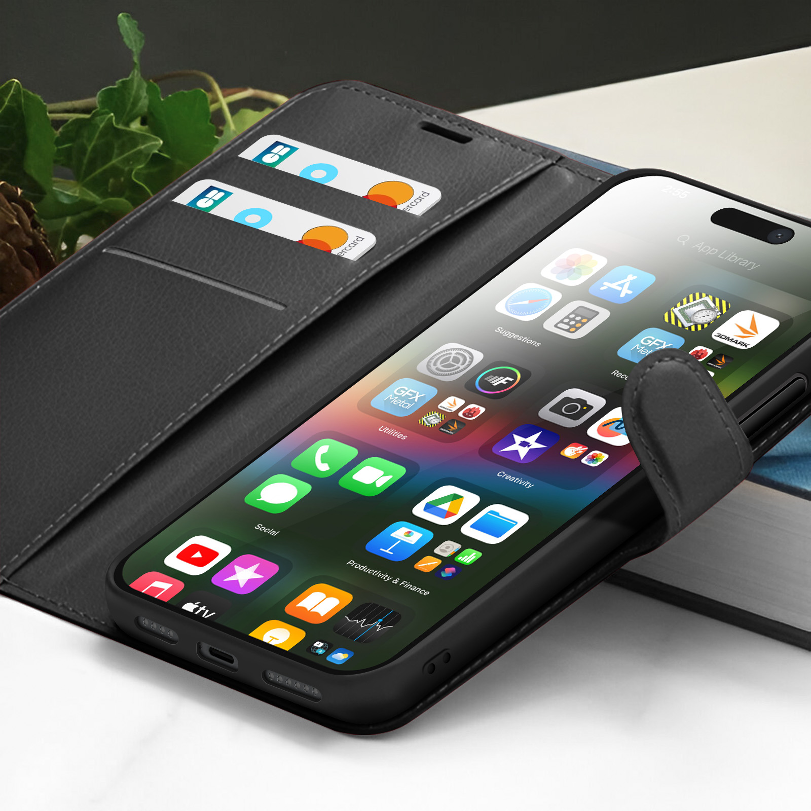 Zwarte telefoonhoes met iPhone. Creditcards binnenin. App-pictogrammen zichtbaar. Achtergrond van groene bladeren.