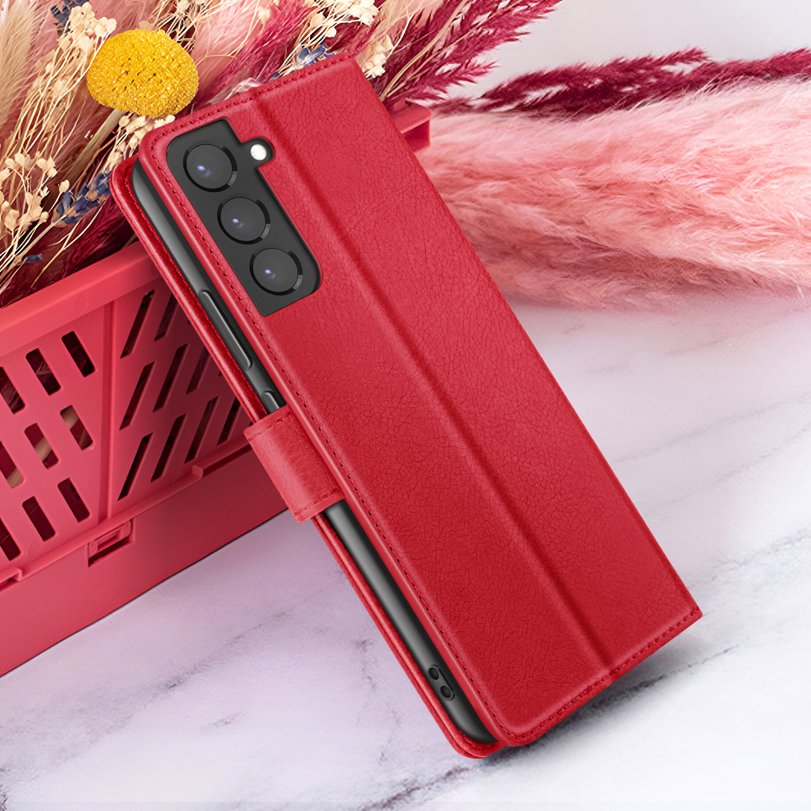 Étui de téléphone rouge avec téléphone noir à l'intérieur. Fleurs roses et rouges en arrière-plan, panier rouge à gauche.