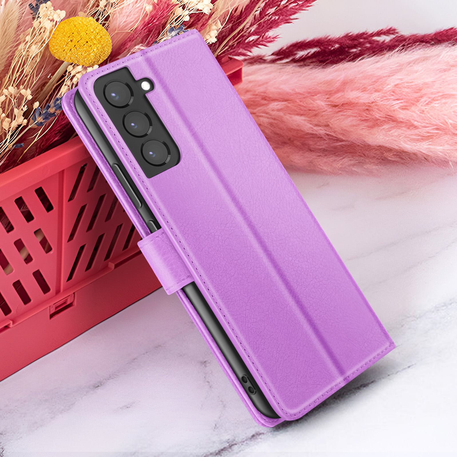 Un étui de téléphone violet avec un téléphone à l'intérieur, posé sur une surface en marbre avec des décorations florales.