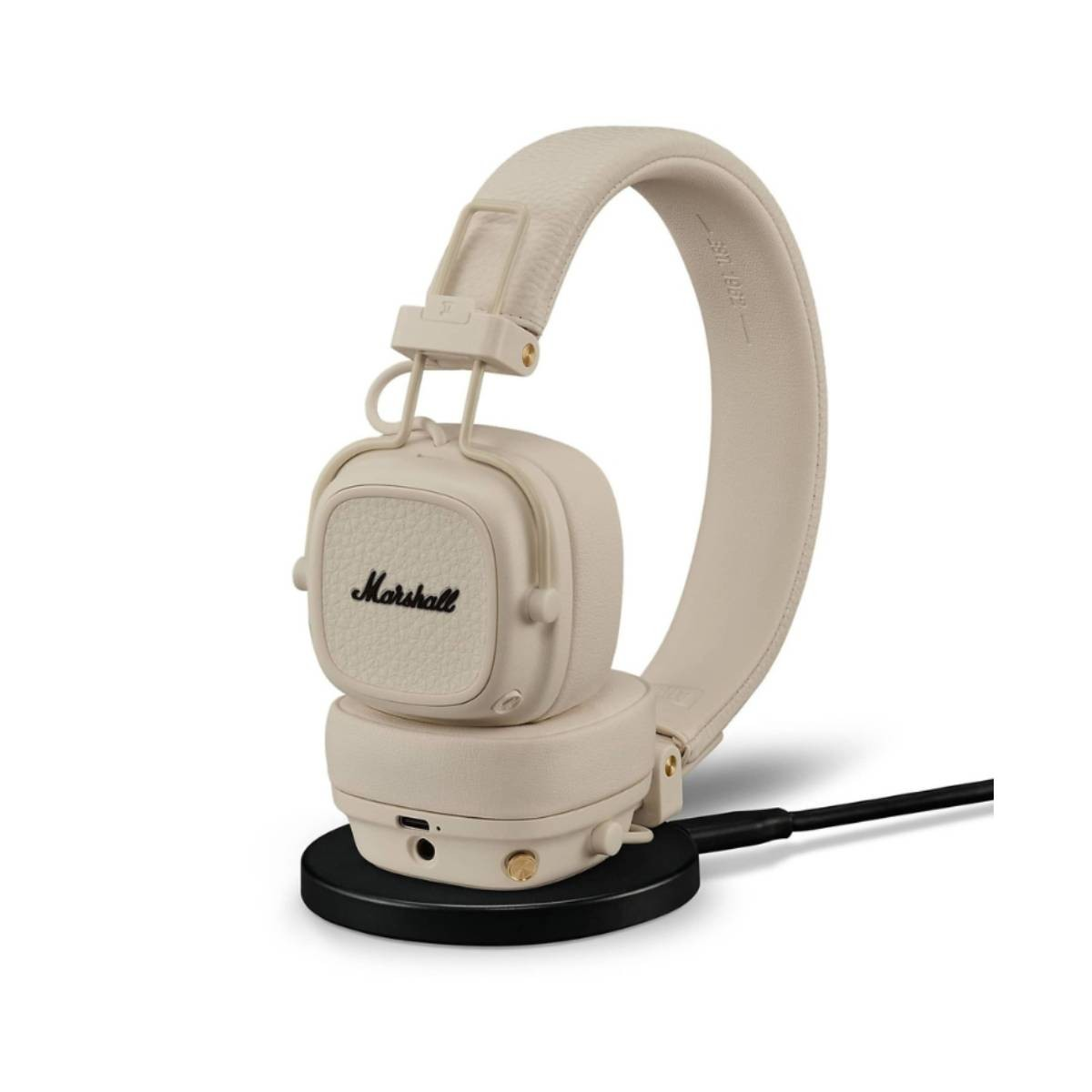 Auriculares Marshall color crema sobre una base de carga negra con cable. Los auriculares tienen el nombre de la marca.
