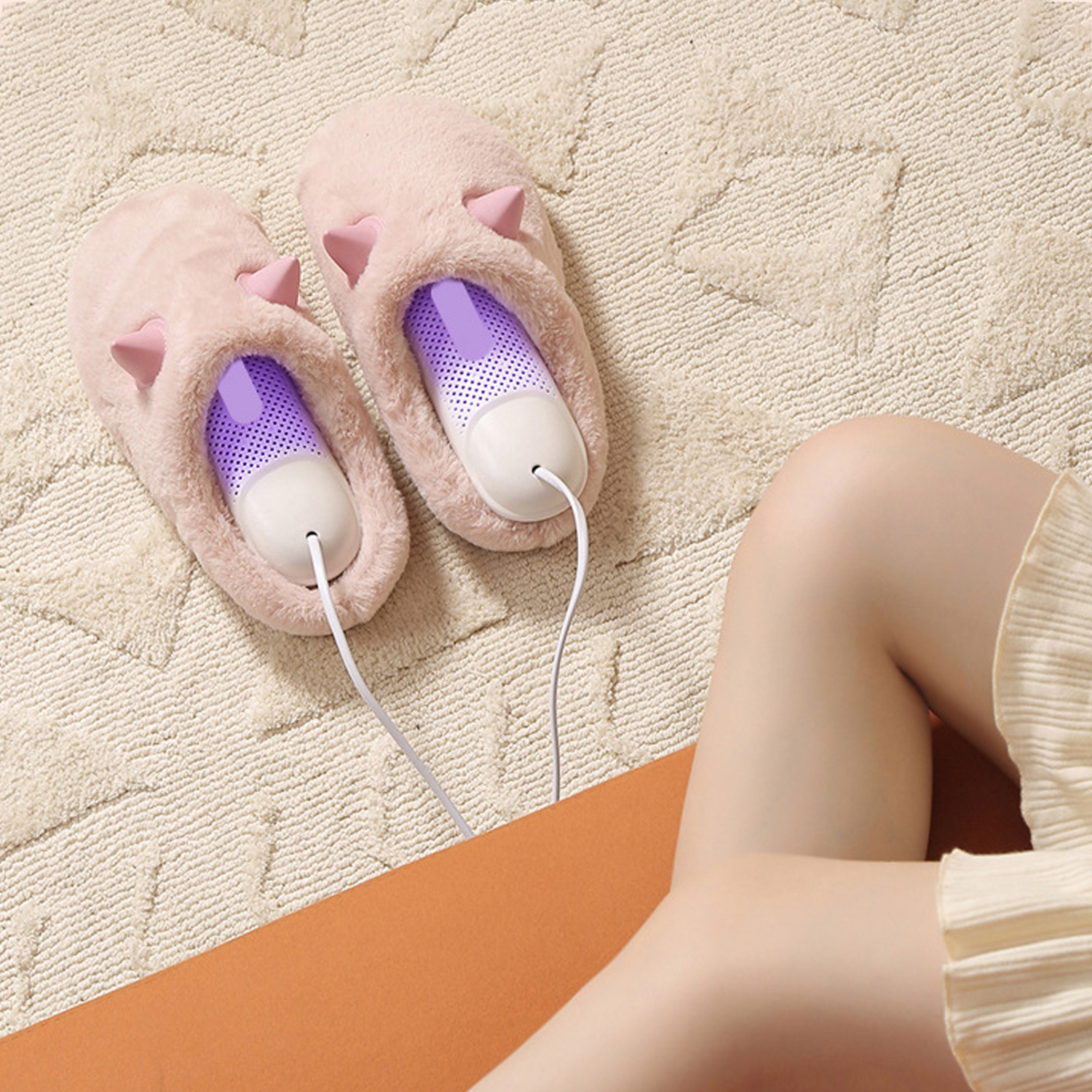 Due pantofole rosa con inserti viola su un tappeto beige, con le gambe di una persona in primo piano. I fili si estendono dalle pantofole.