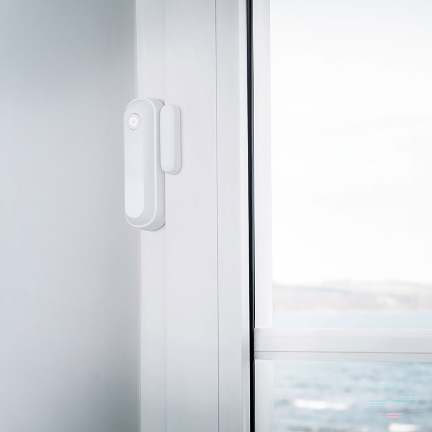 Biały czujnik okienny jest przymocowany do białej ramy okiennej. Okno jest otwarte, pokazując widok na zewnątrz.