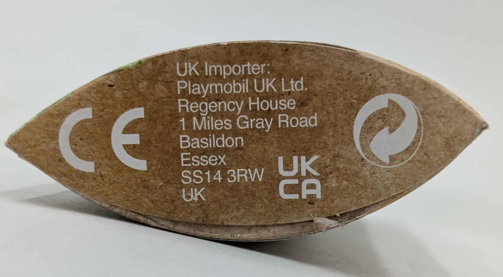 A brown cardboard box with text and symbols. The text includes the UK importer's address and CE mark.