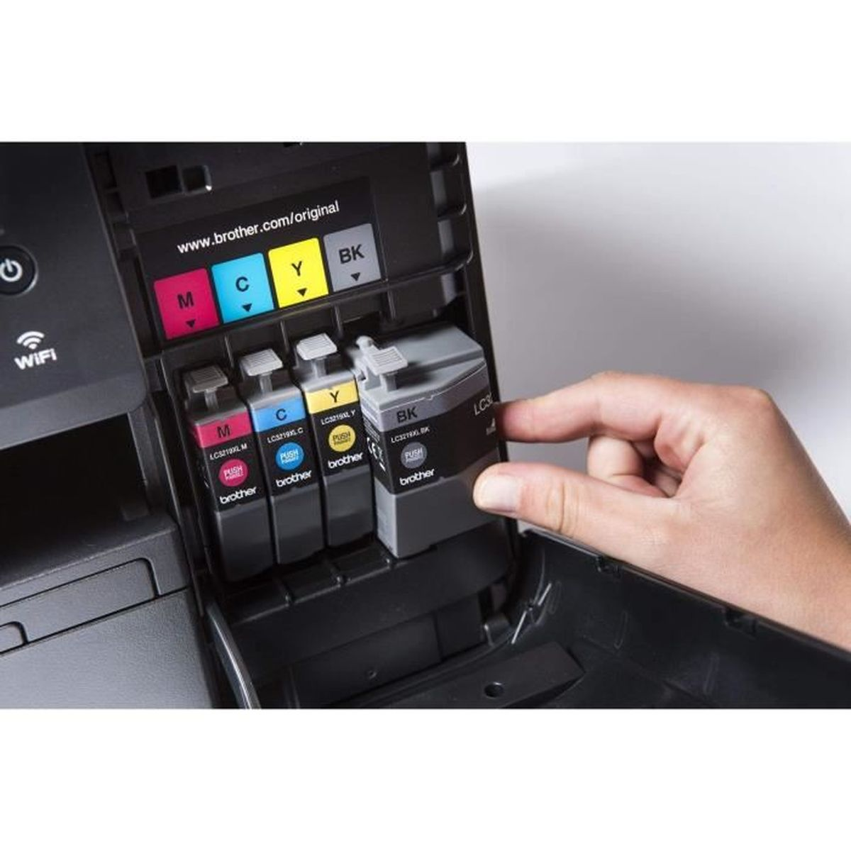 Ręka wkłada czarny wkład atramentowy do drukarki Brother. Drukarka ma gniazda na wkłady cyjan, magenta, żółty i czarny.