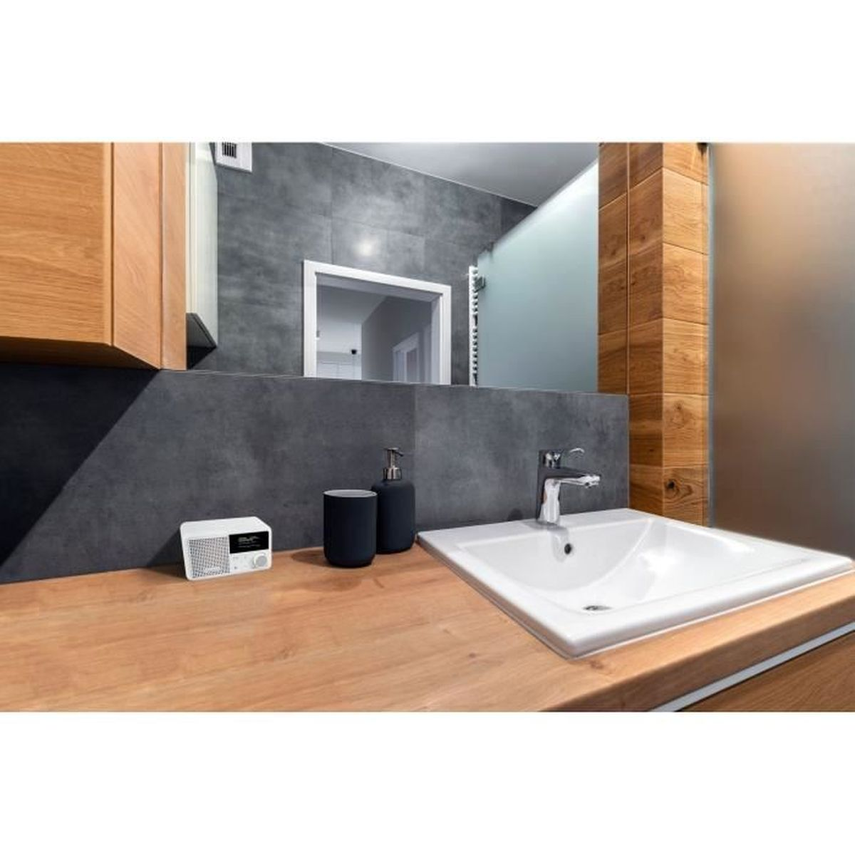 Bathroom with a white sink, chrome faucet, wooden countertop, mirror. Soap dispenser, cup, and radio sit on the counter.