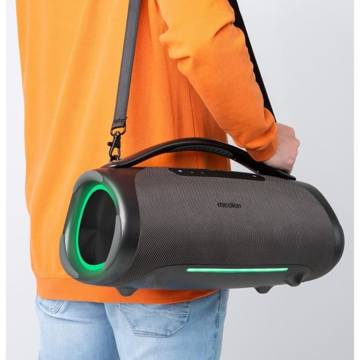 Een persoon houdt een grote, grijze luidspreker vast met een zwarte handgreep en riem. De luidspreker heeft groene lichten. De persoon draagt ​​oranje en een spijkerbroek.