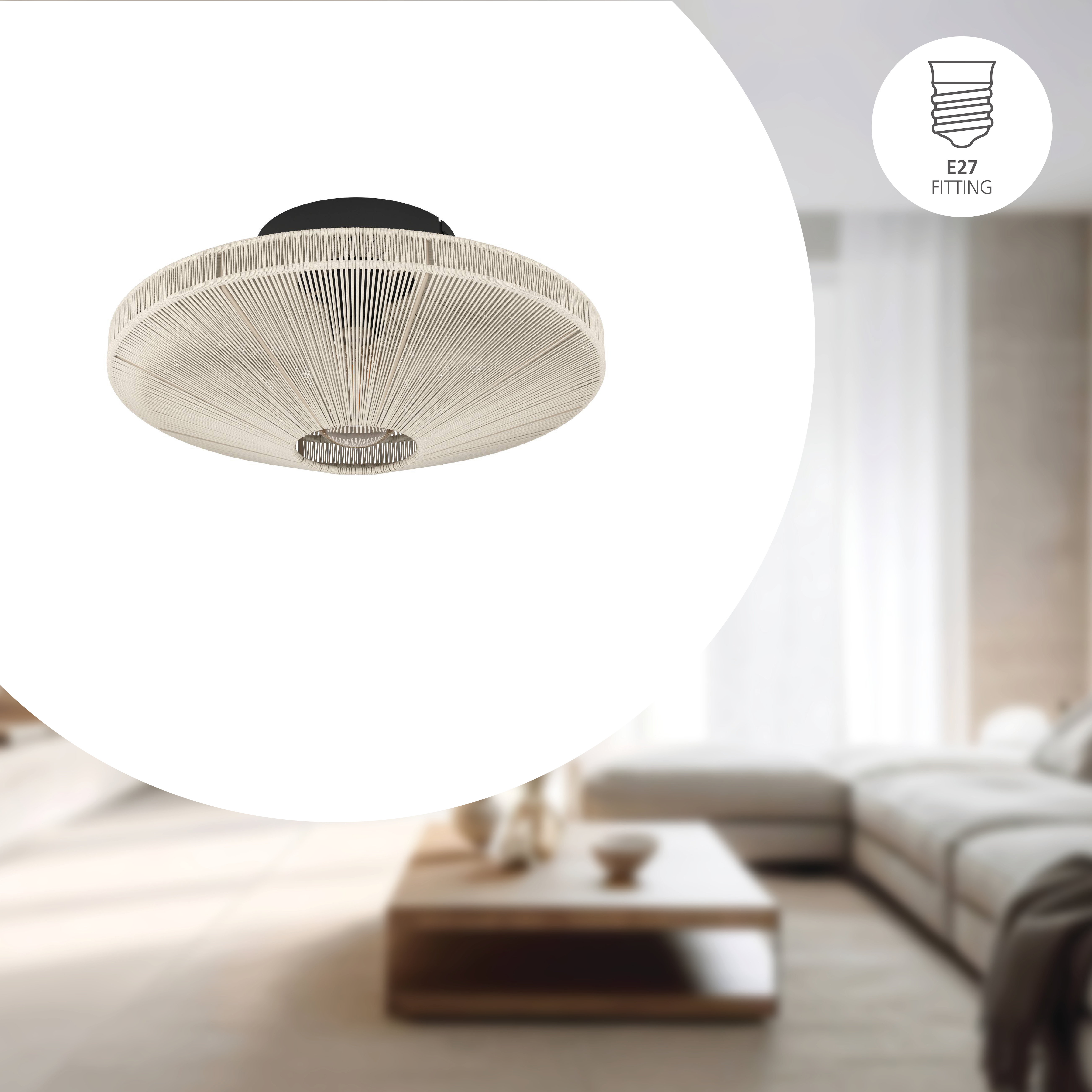 Una lampada da soffitto beige, circolare e intrecciata. Lo sfondo mostra un soggiorno sfocato con un divano e un tavolino.