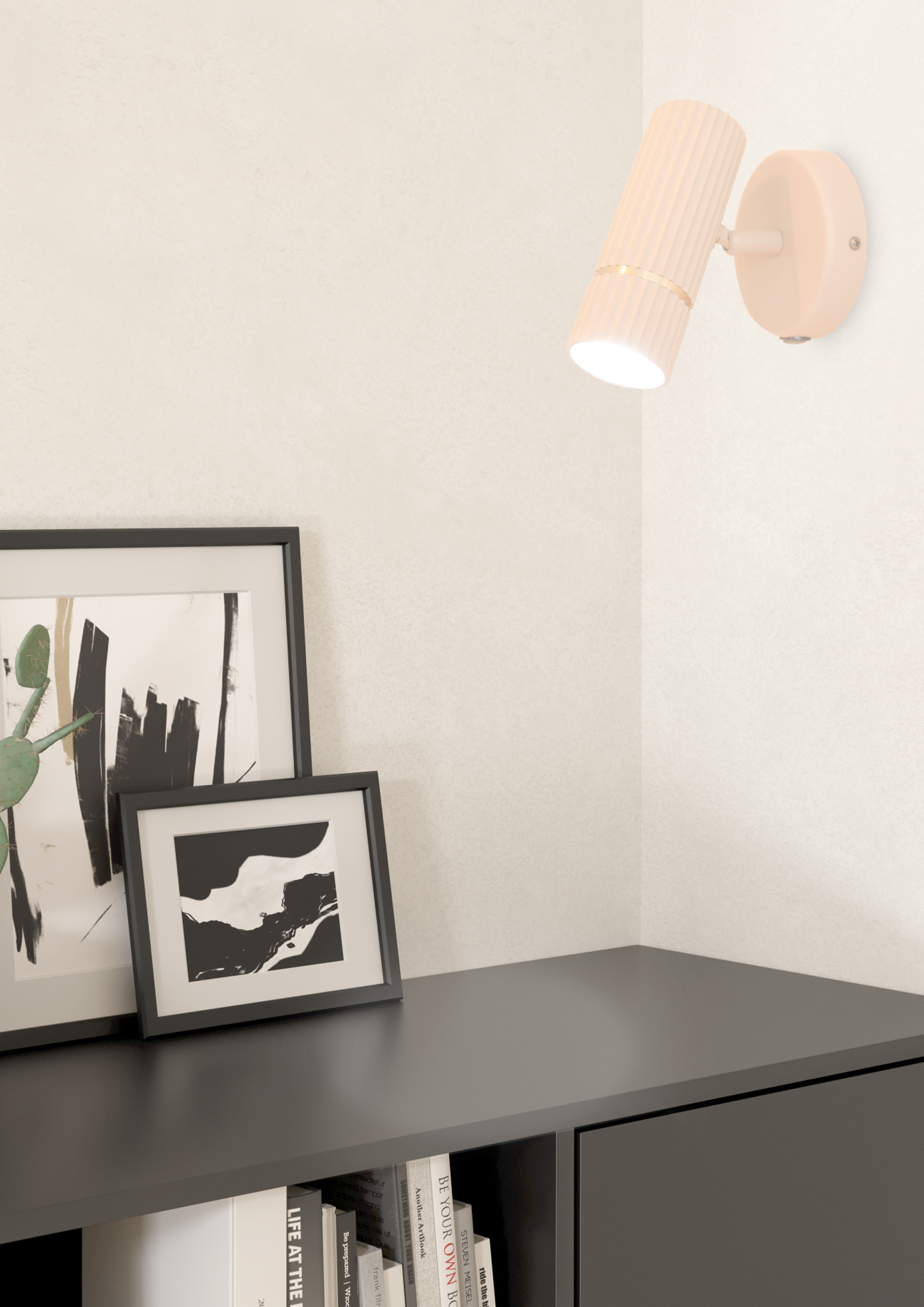 Una lampada da parete è sul muro, e sotto c'è un tavolo nero con quadri incorniciati. Sotto il tavolo ci sono dei libri.