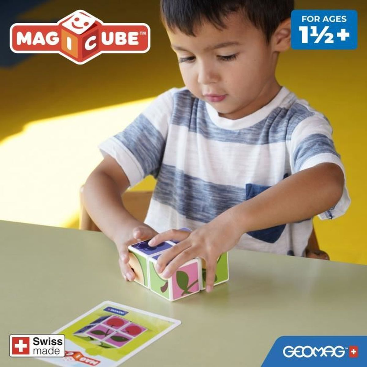 Un bambino gioca con un giocattolo a cubo colorato su un tavolo. Il giocattolo ha lati di diversi colori con immagini. C'è anche una carta sul tavolo.