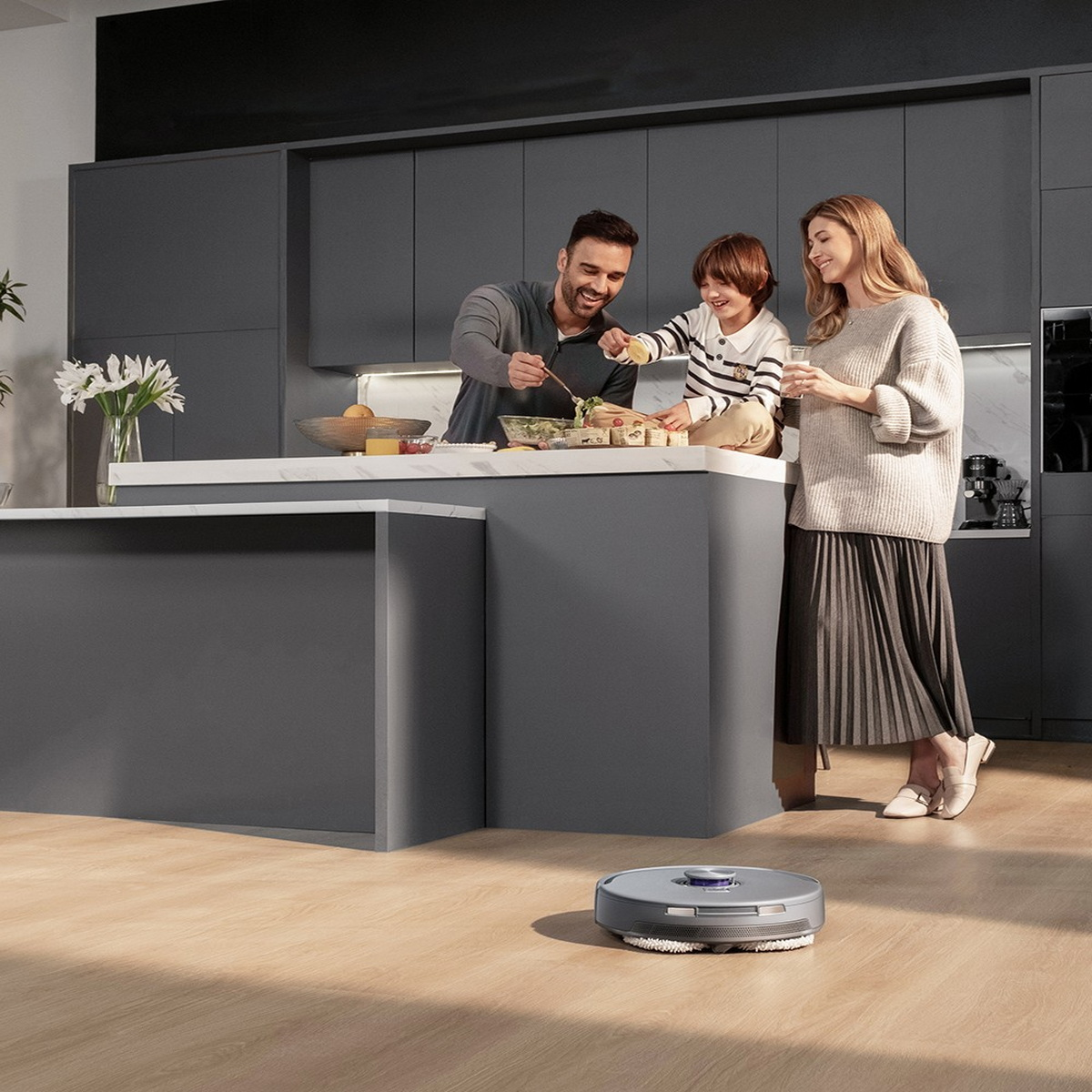 Familie in einer modernen Küche beim Kochen. Ein Roboter-Staubsauger steht auf dem Holzboden. Eine Familie kocht.