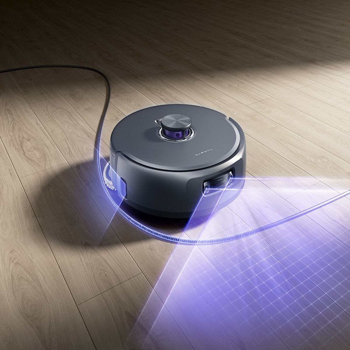 Ein dunkelgrauer Roboter-Staubsauger auf Holzboden. Ein violettes Licht wird vom Staubsauger emittiert. Ein Kabel ist mit dem Staubsauger verbunden.