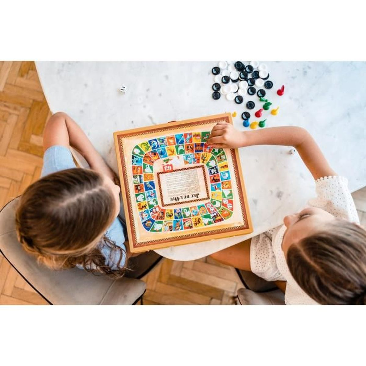 Zwei Kinder spielen ein Brettspiel auf einem Marmortisch. Würfel und Spielfiguren sind in der Nähe verstreut. Das Brett ist bunt mit Bildern.