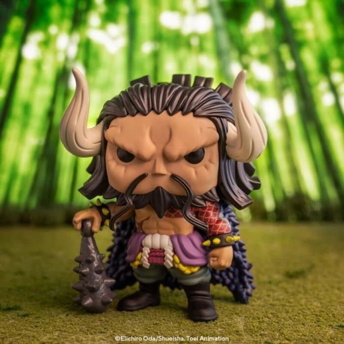 Figurka Funko Pop Kaido. Ma rogi, brodę i trzyma kolczasty kij. Tło to drzewa bambusowe.