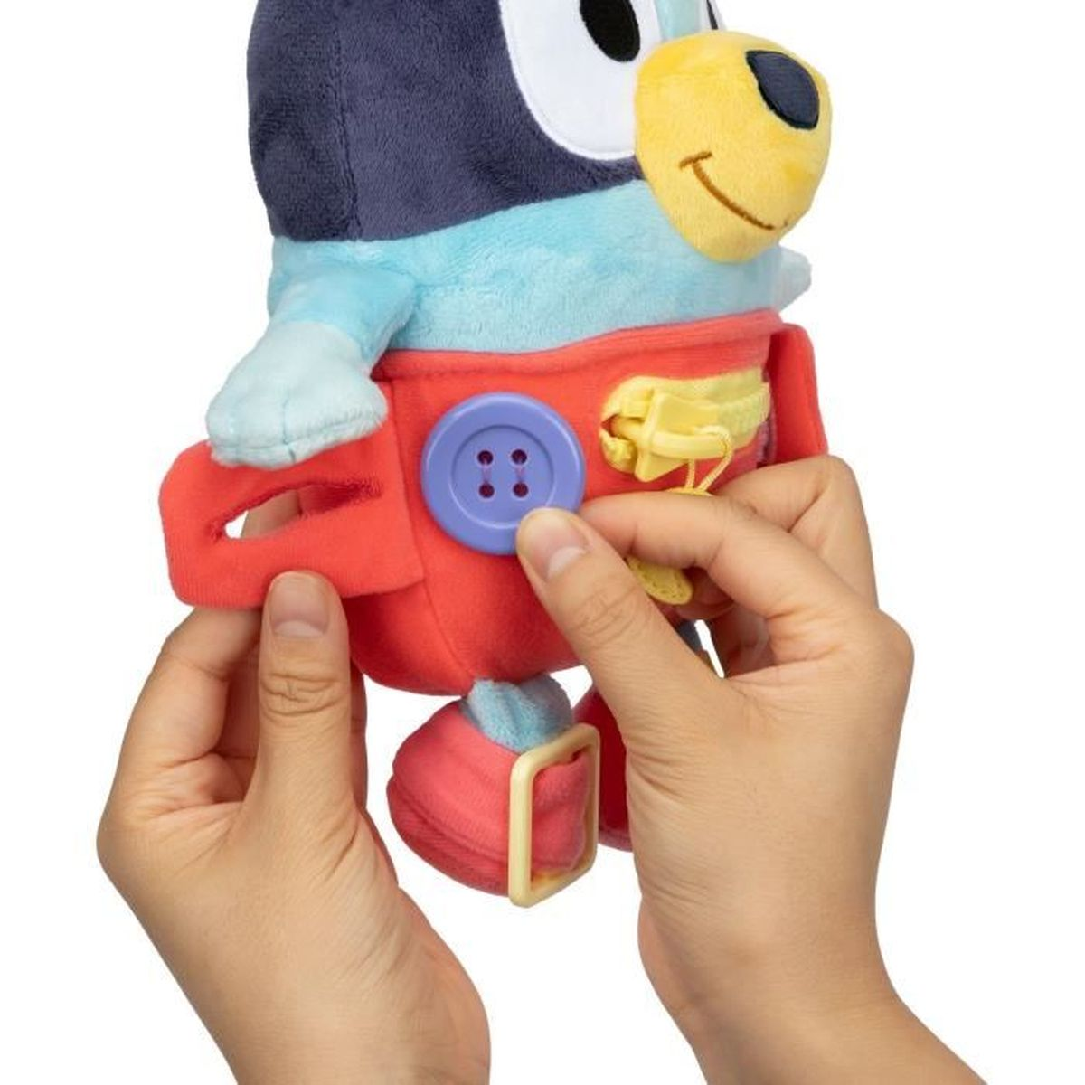 Mains tenant un jouet en peluche d'un personnage aux couleurs bleu, rouge et jaune. Le jouet a des boutons et des fermetures éclair.