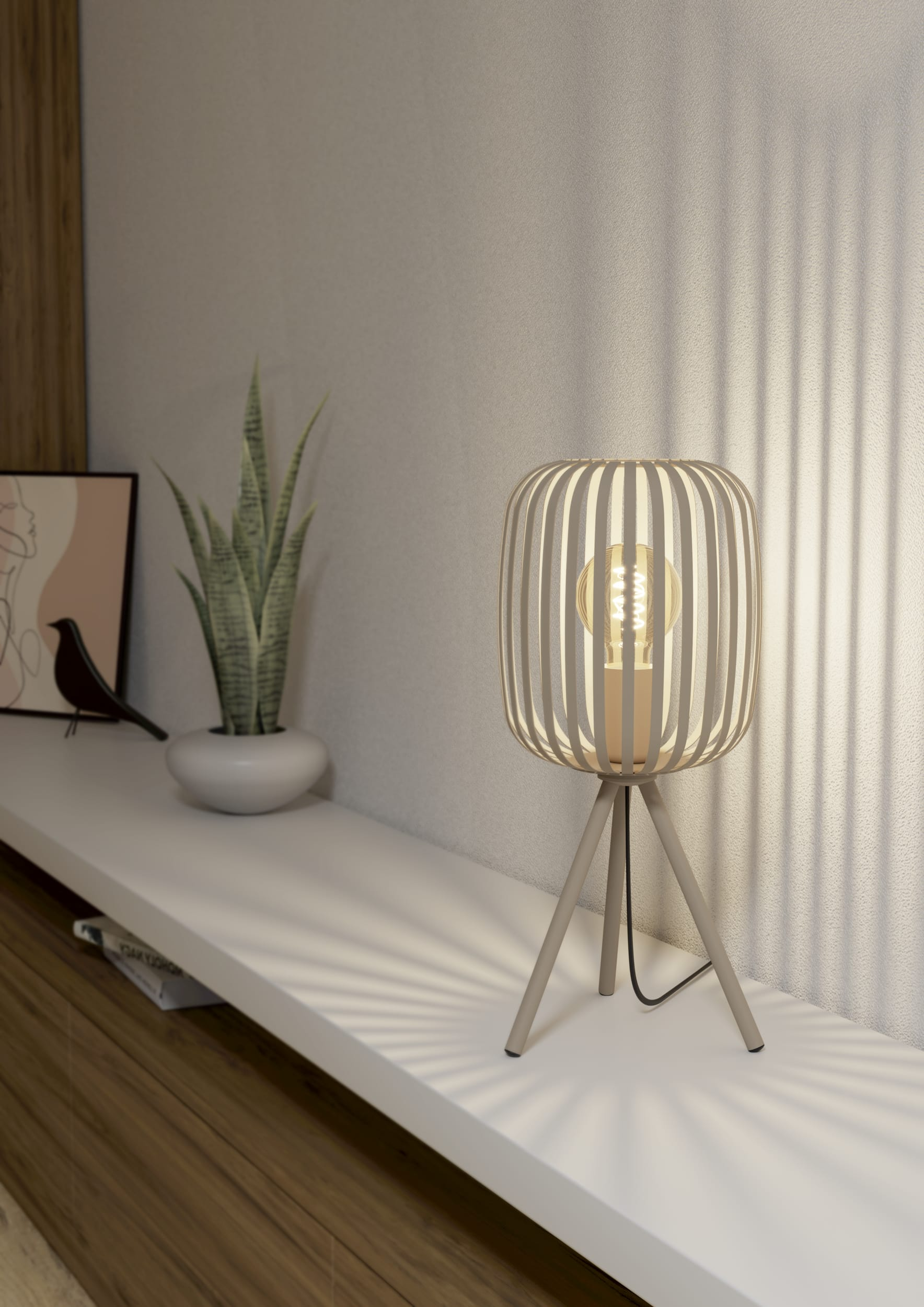Een lamp met een kooivormige kap staat op een witte plank. Een plant en kunstwerk staan ook op de plank.