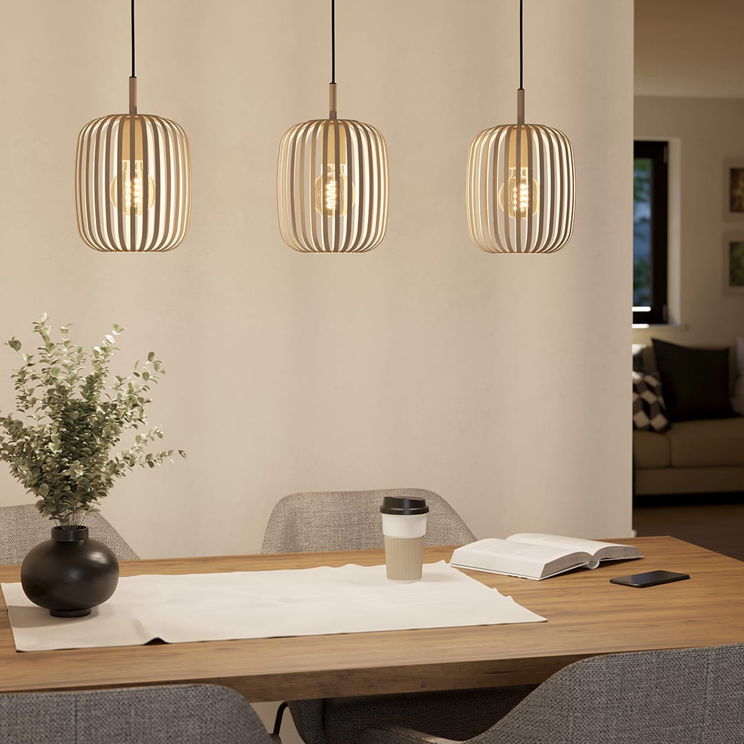 Drie hanglampen boven een tafel. Op de tafel: vaas met planten, koffiekopje, boek en telefoon.