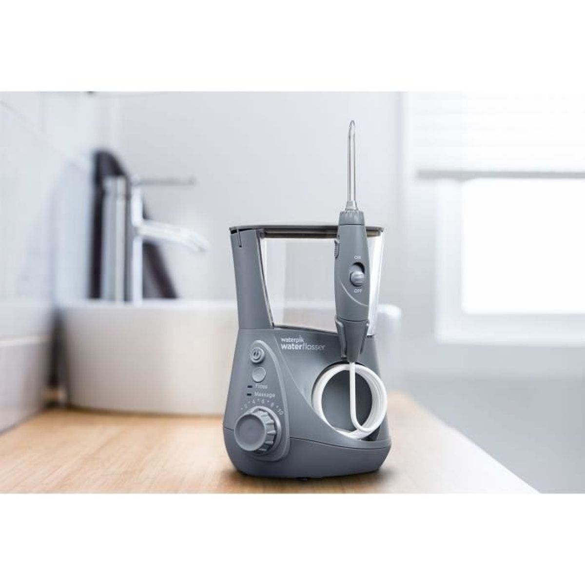 Ein grauer Waterpik-Wasserflosser steht auf einer Holzoberfläche in einem Badezimmer. Im Hintergrund sind ein Waschbecken und ein Fenster zu sehen.