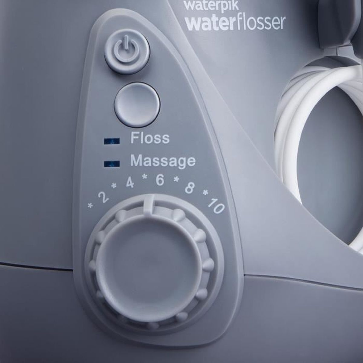 Nahaufnahme eines grauen Waterpik-Wasserflosser-Bedienfelds. Es hat Ein-/Aus- und Modustasten sowie einen Drehregler für die Intensitätseinstellungen.