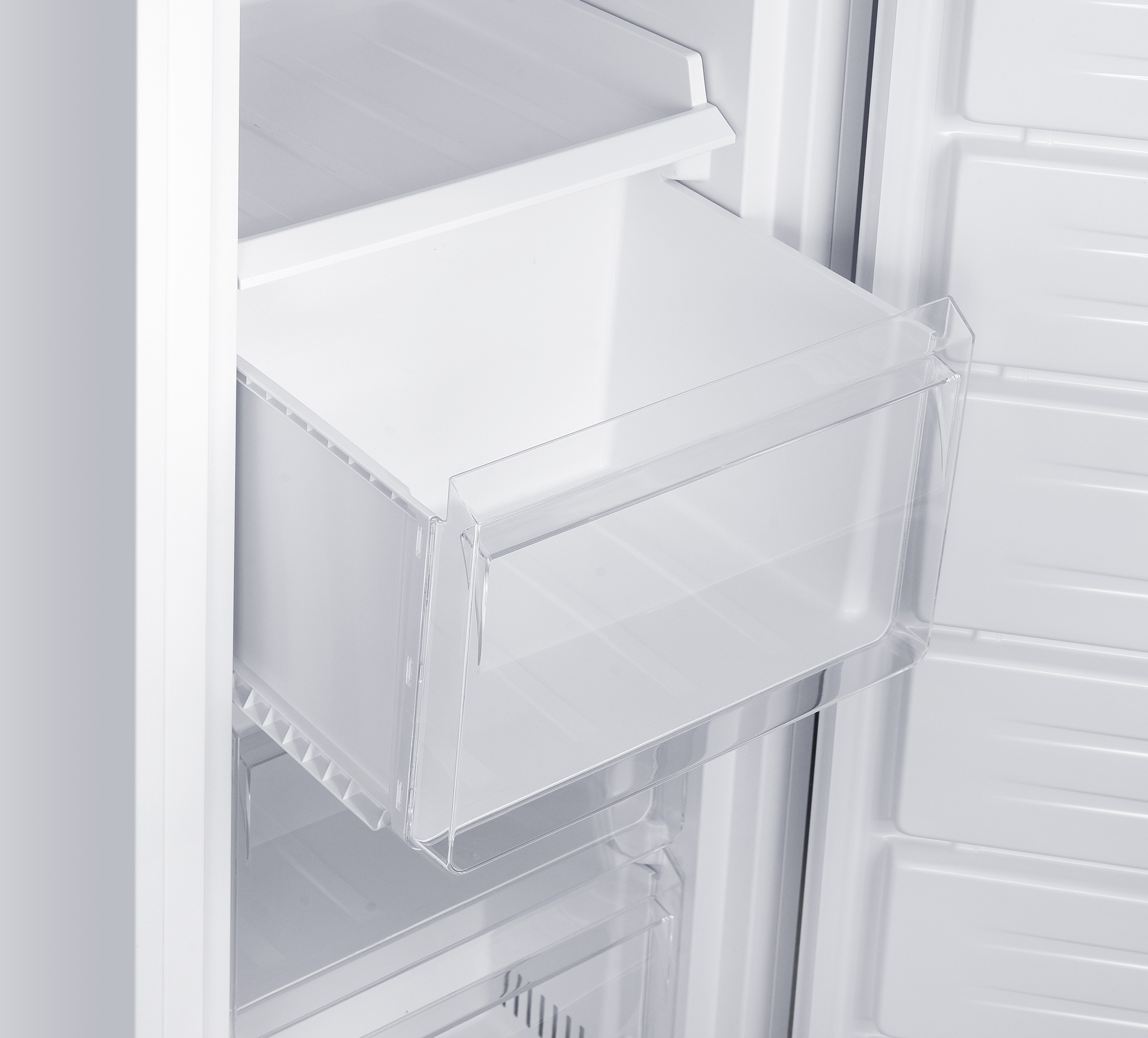 In einem weißen Kühlschrank sind eine offene Schublade und Regale zu sehen. Die Schublade hat eine transparente Kunststofffront.