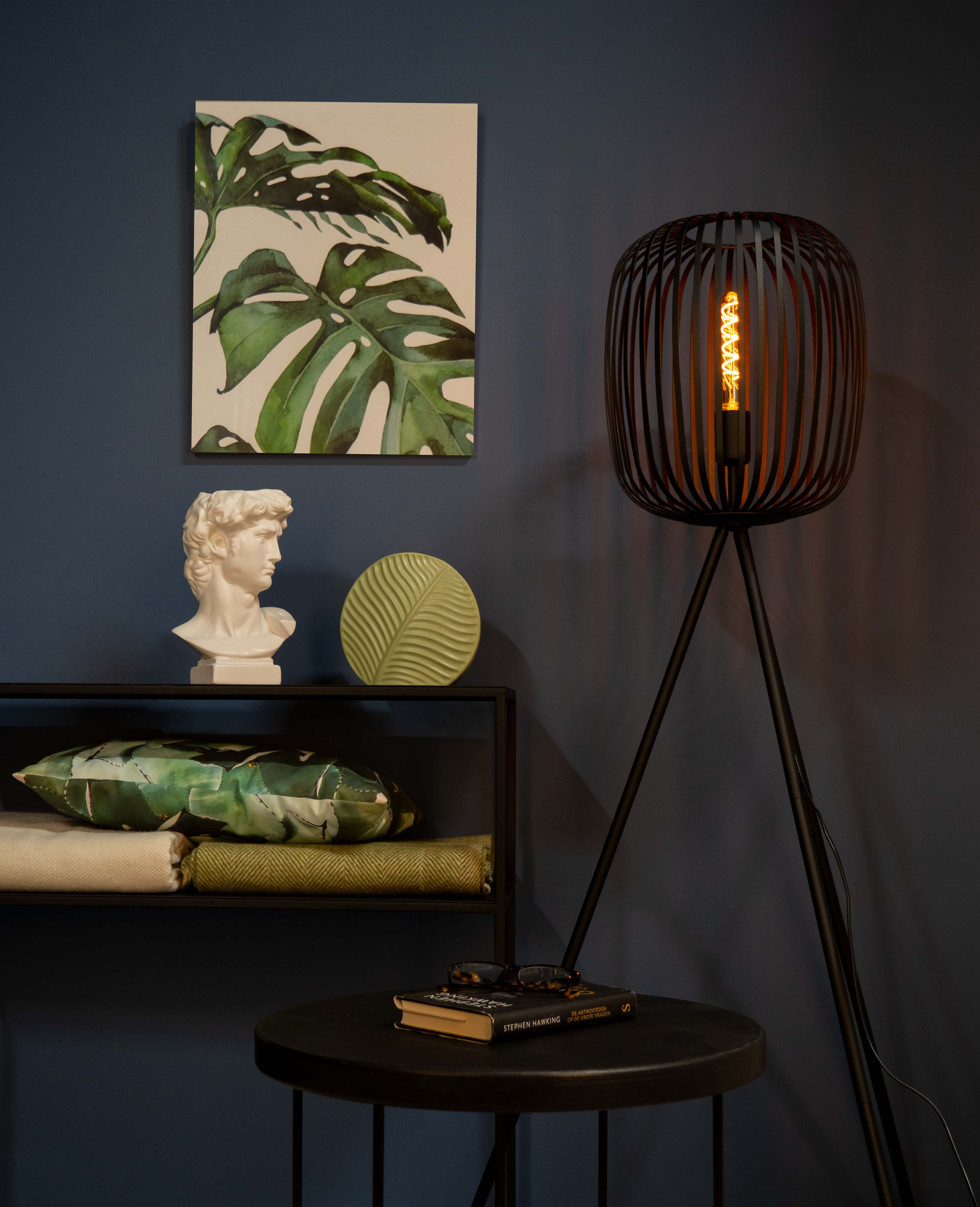 Een kamer met een schilderij, een buste, een lamp en een bijzettafel met een boek en een bril.