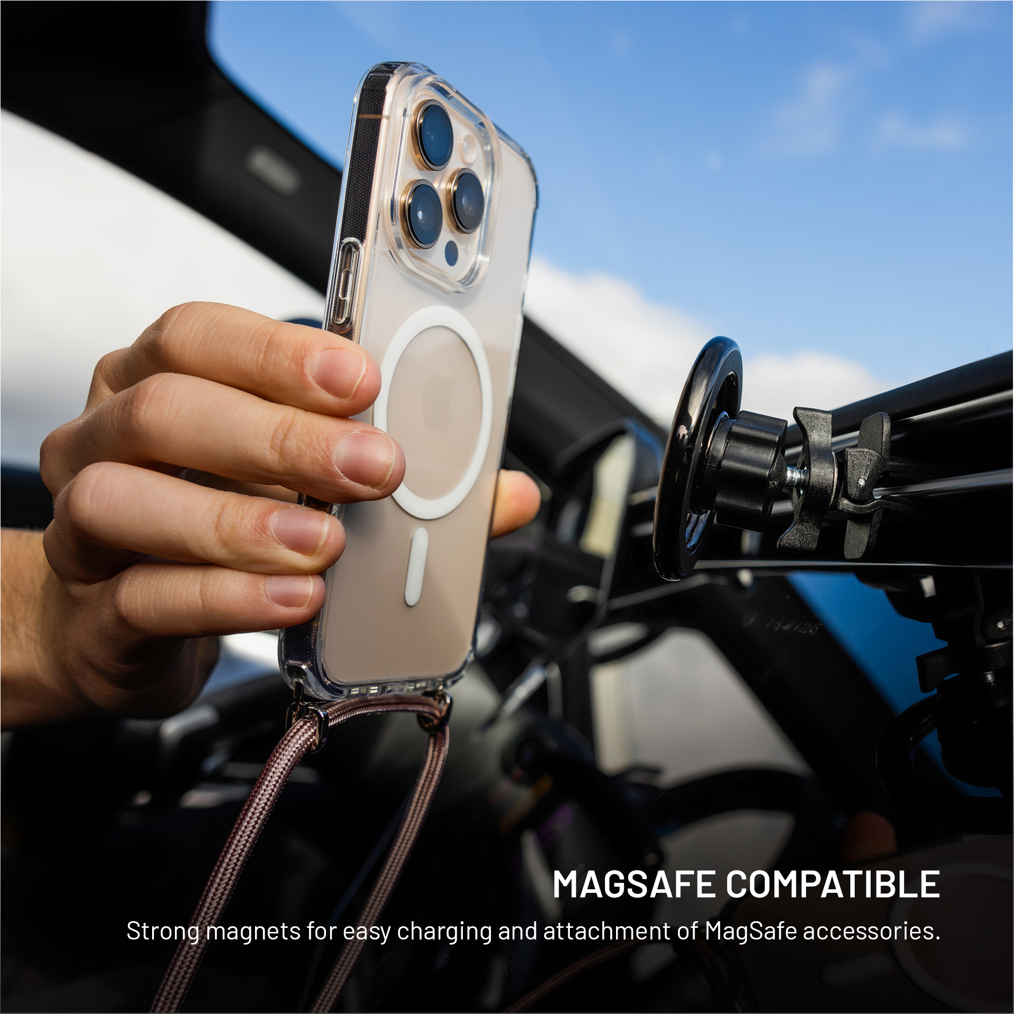 Eine Hand hält ein Telefon in einer transparenten Hülle in einem Auto. Der Hintergrund ist blauer Himmel und Autoteile.