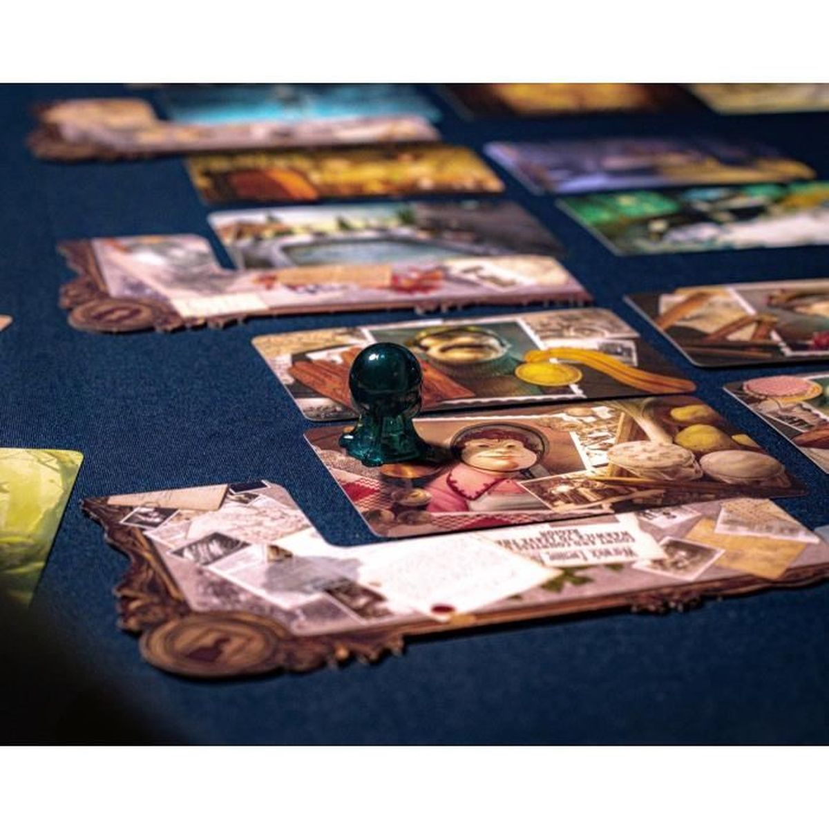 Brettspiel-Setup. Karten mit Bildern, ein grünes Spielteil, und eine dunkelblaue Oberfläche. Fokus auf die Komponenten.
