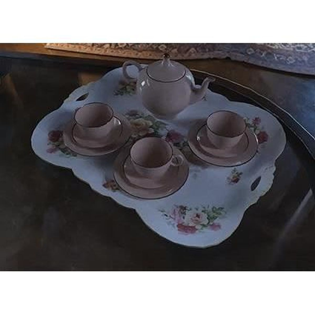 Ein Teeservice auf einem floralen Tablett. Es enthält eine Teekanne, drei Tassen und Untertassen. Das Set ist rosa, mit einem weißen, floralen Tablett.