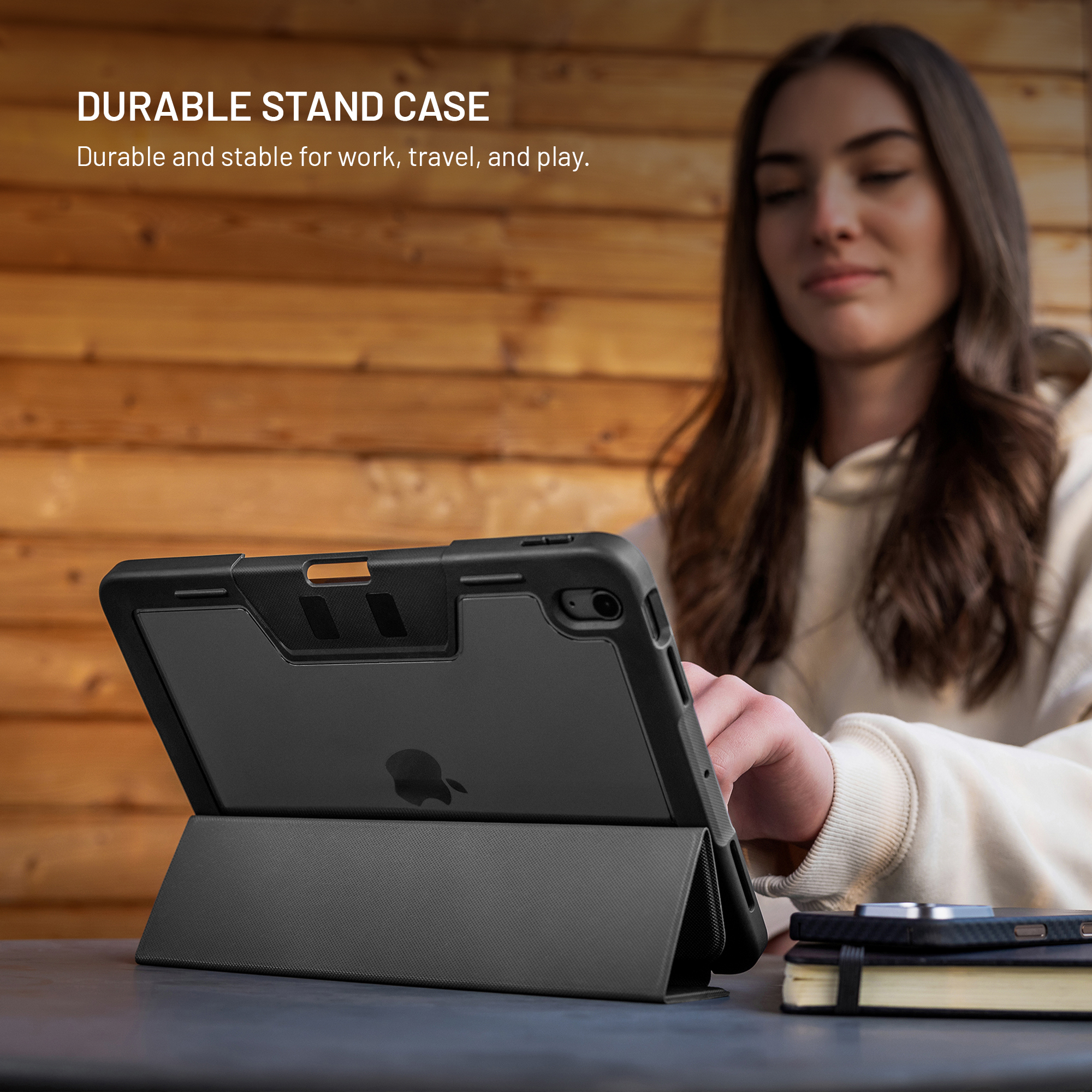 Eine Frau benutzt eine schwarze Tablethülle. Das Tablet liegt auf einem Tisch mit einem Notizbuch und einem Telefon. Holz-Hintergrund.