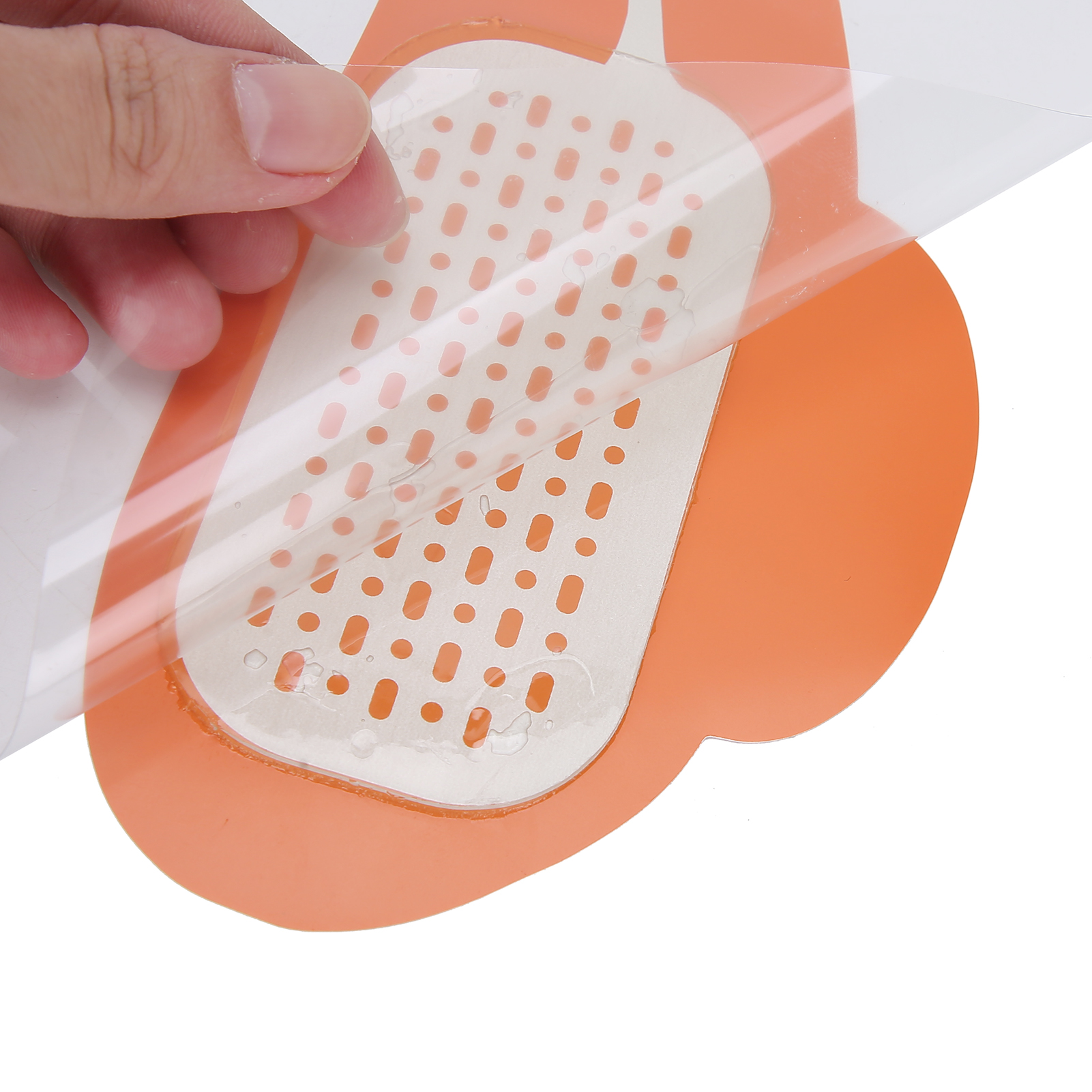 Hand zieht transparente Folie von orangefarbenem Pad mit perforiertem Muster ab. Weißer Hintergrund.