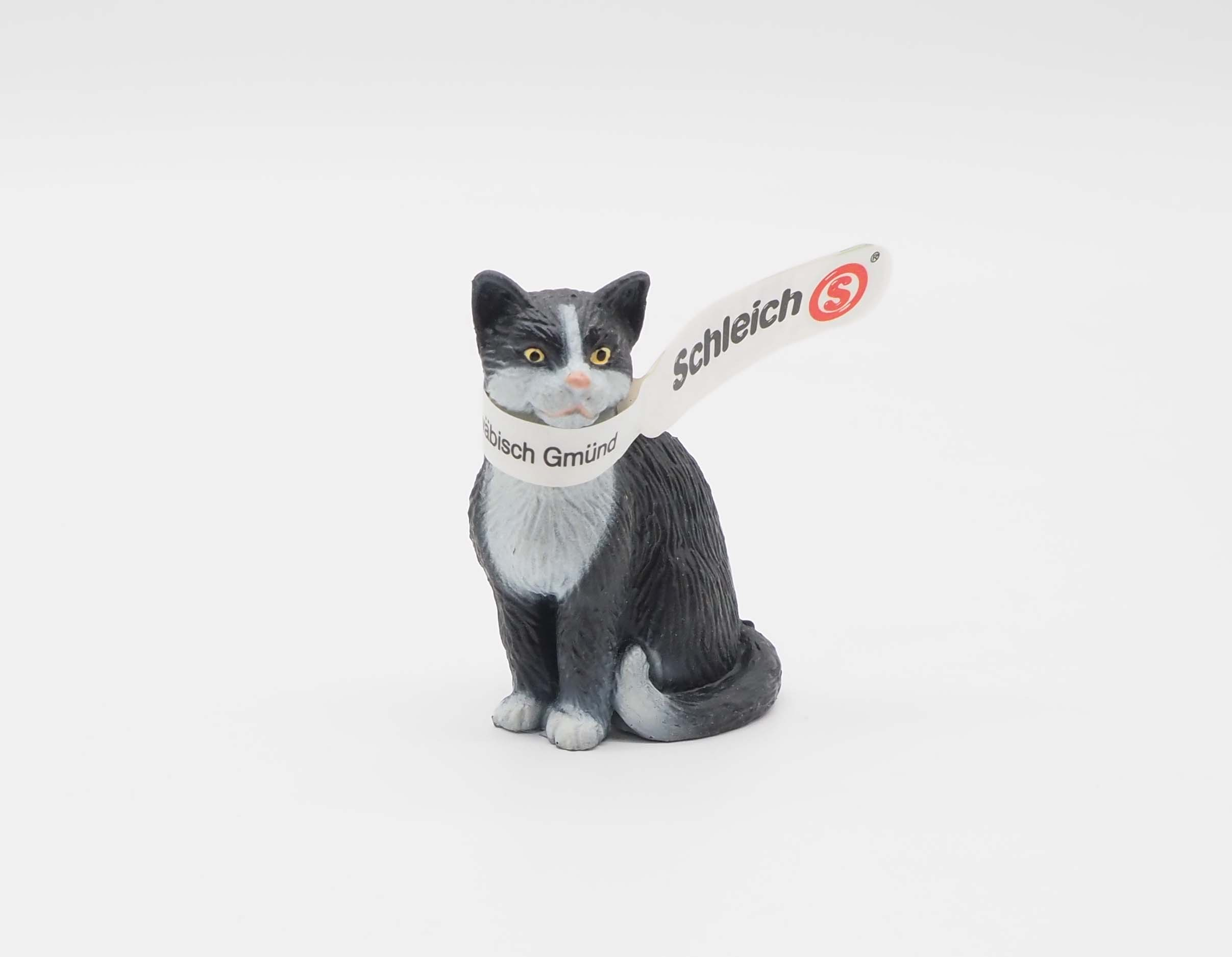 Eine schwarz-weiße Katzenfigur mit einem Anhänger der Firma 'Schleich'. Der Hintergrund ist weiß.