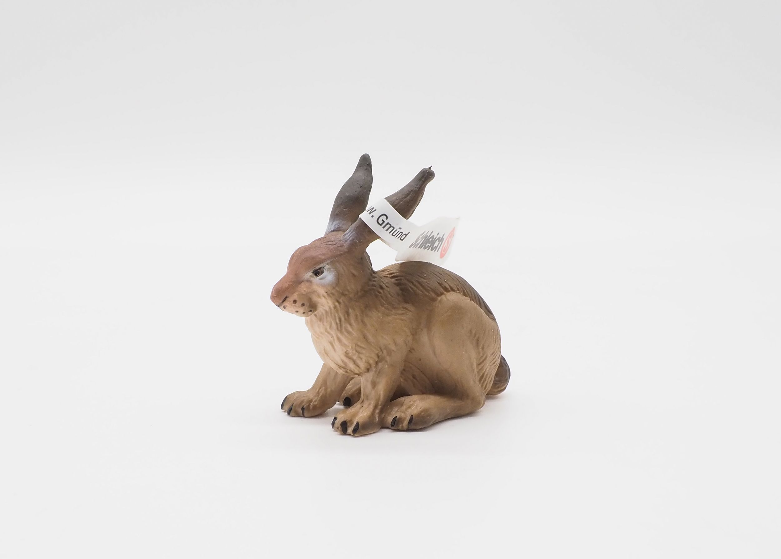 Eine braune Hasenfigur mit langen Ohren und einem Etikett auf weißem Hintergrund.