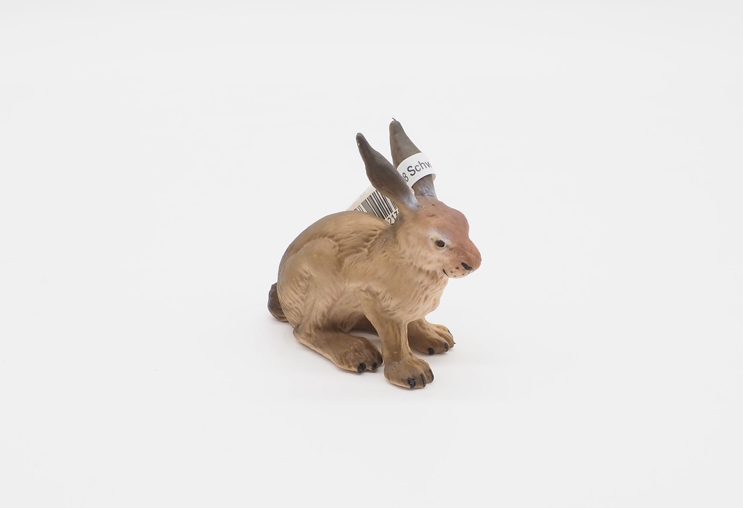 Eine braune Hasenfigur mit schwarzen Ohren und einem Etikett auf weißem Hintergrund. Der Hase sitzt.