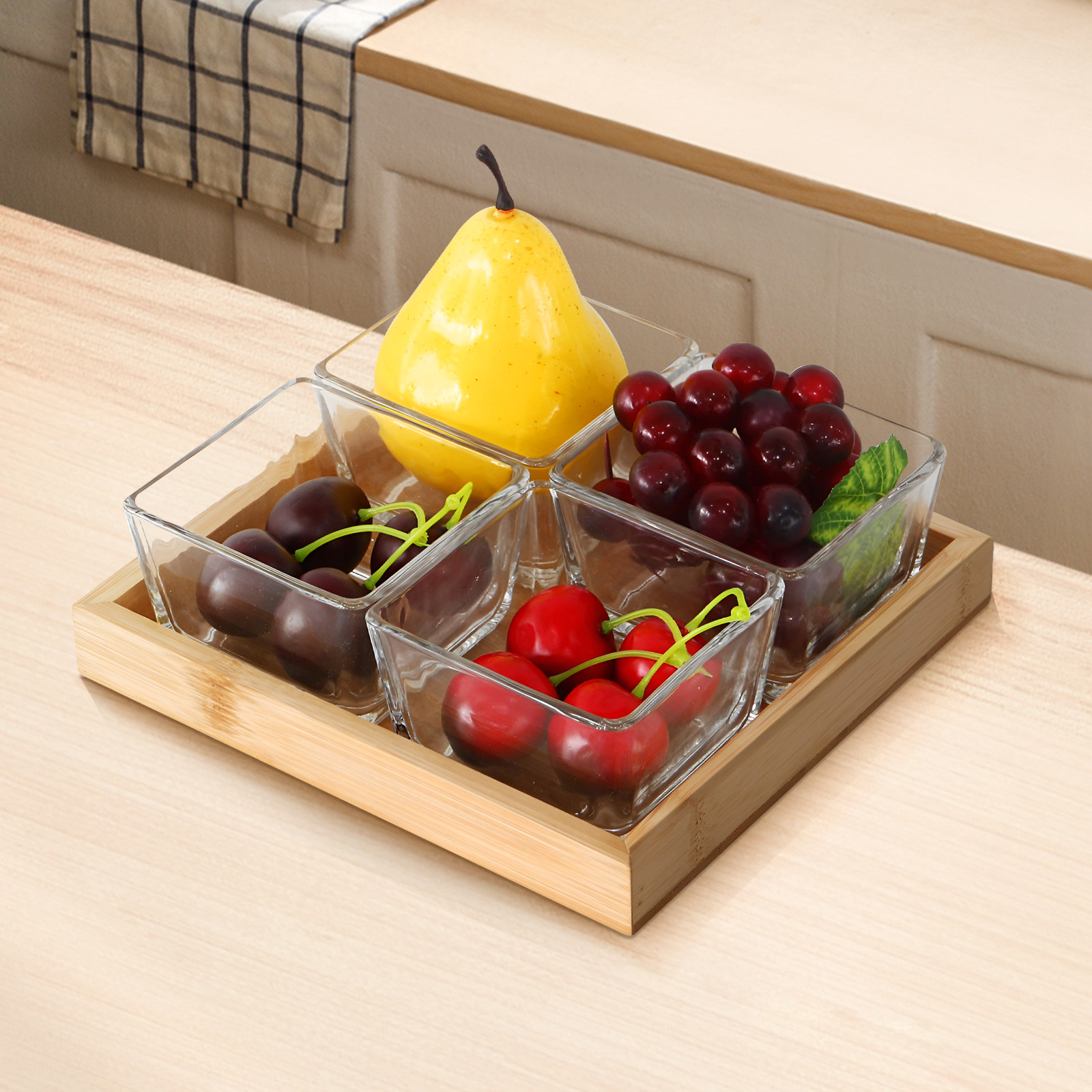 Ein Holztablett mit vier Glasbehältern mit gelber Birne, roten Kirschen, dunklen Trauben und schwarzen Kirschen.