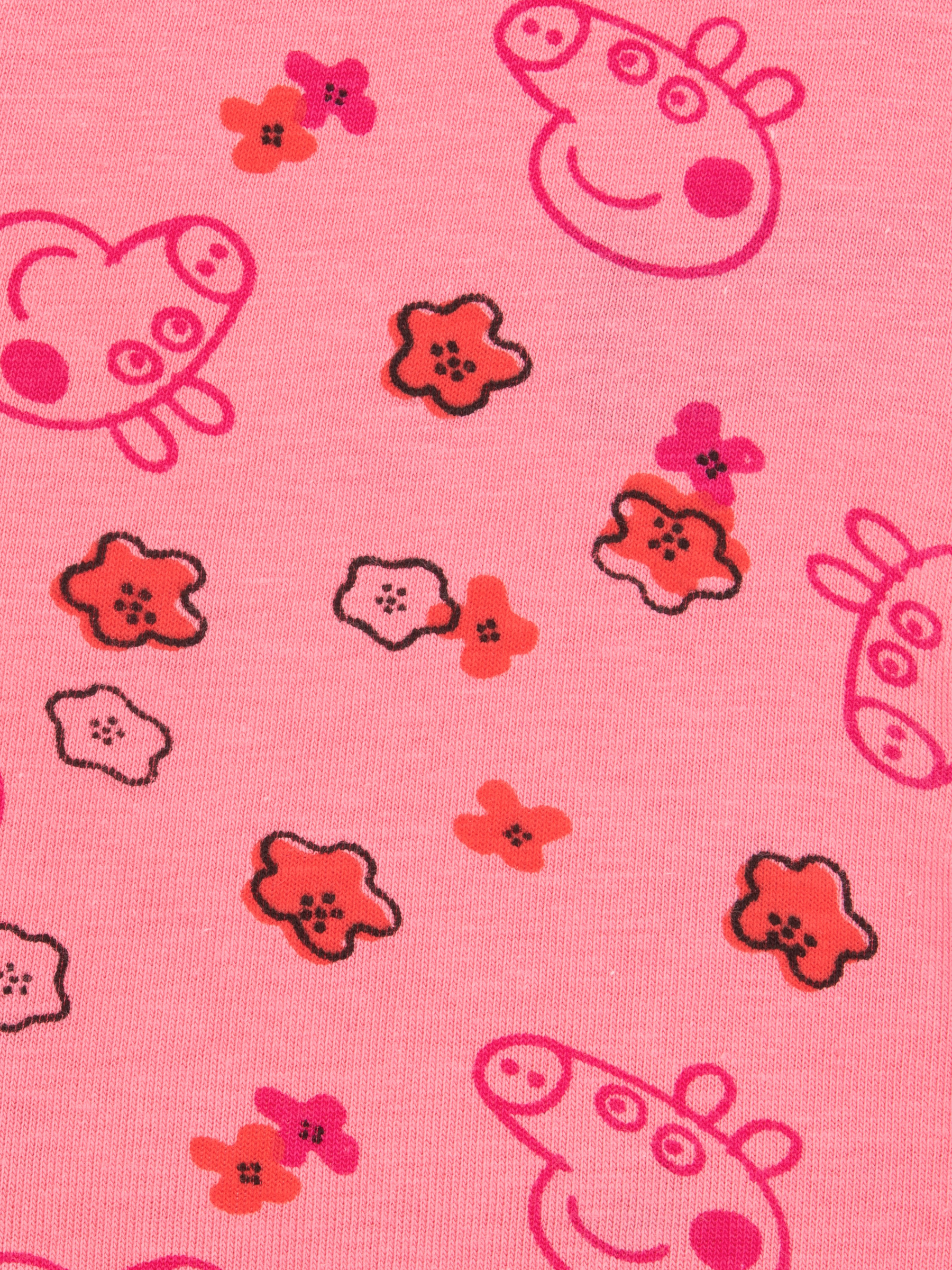 Rosa Stoff mit Peppa Wutz Gesichtern und roten Blumenmustern. Der Hintergrund ist einfarbig rosa.