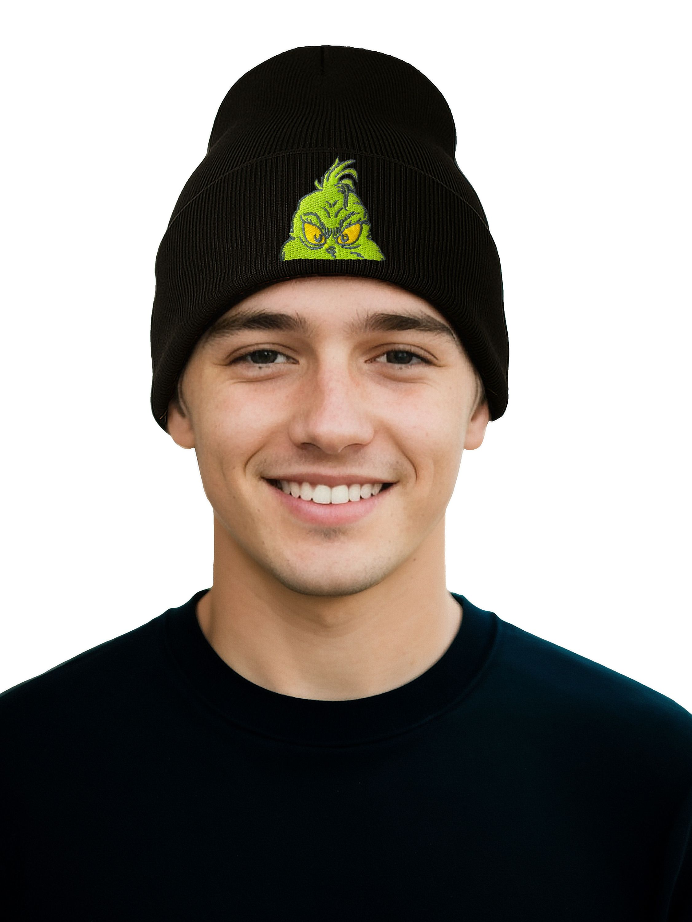 Ein junger Mann lächelt und trägt eine schwarze Mütze mit Grinch-Gesicht. Er hat ein schwarzes Hemd, weißer Hintergrund.