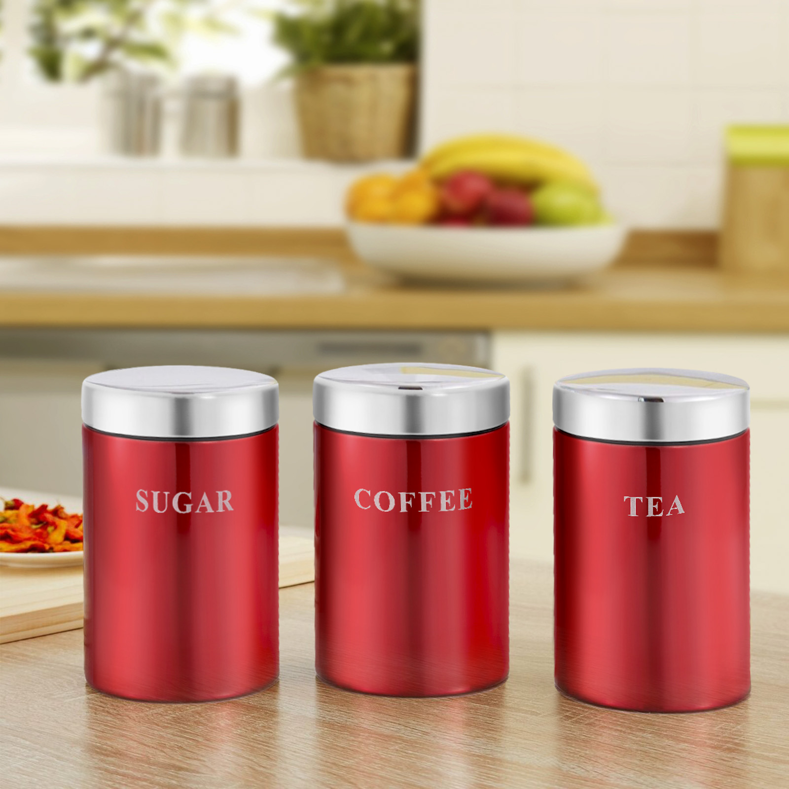 Drei rote Behälter mit der Aufschrift Zucker, Kaffee und Tee mit silbernen Deckeln auf einer Holztheke. Ein verschwommener Küchenhintergrund ist sichtbar.