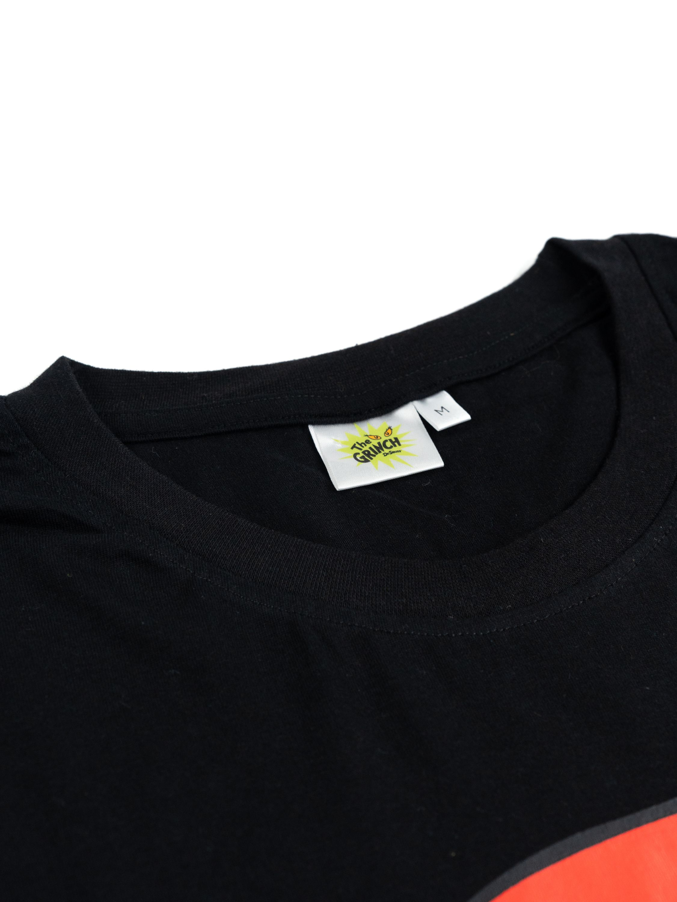 Schwarzes T-Shirt mit einem Etikett mit dem Logo 'The Grinch'. Der Halsausschnitt des Shirts ist sichtbar, am unteren Rand ist ein Hauch von Rot zu sehen.