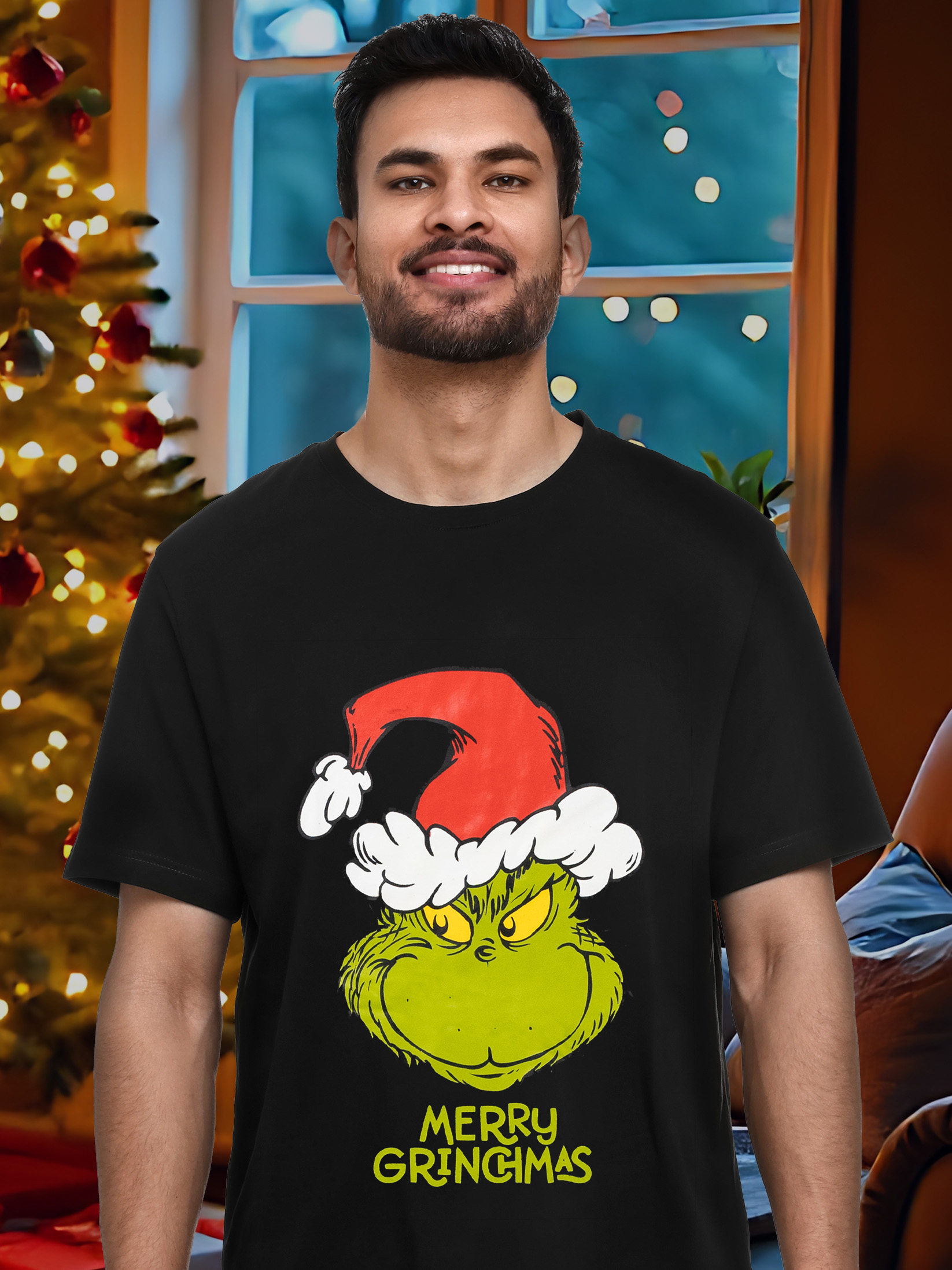 Mann trägt ein schwarzes 'Merry Grinchmas'-Shirt und lächelt. Ein Weihnachtsbaum ist hinter ihm. Der Hintergrund hat ein Fenster.