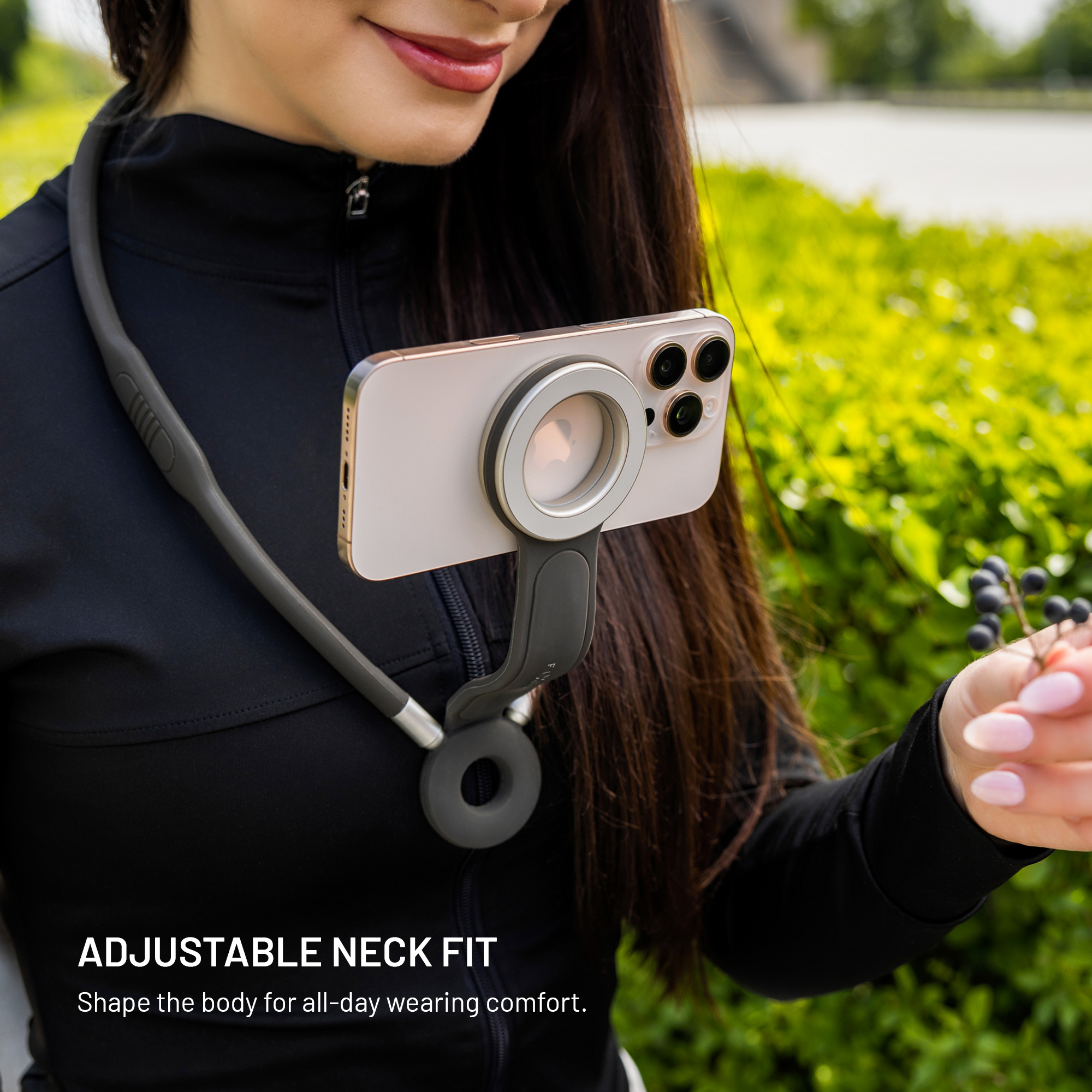 Eine Frau, die einen Nacken-Telefonhalter trägt und schwarze Beeren hält, mit grünem Laub im Hintergrund.
