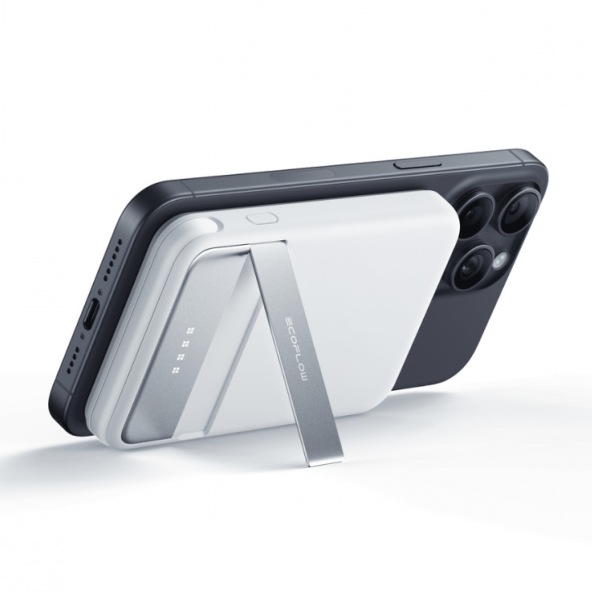 Czarny smartfon jest podparty przez białą przenośną ładowarkę ze srebrną podstawką. Tło jest białe.