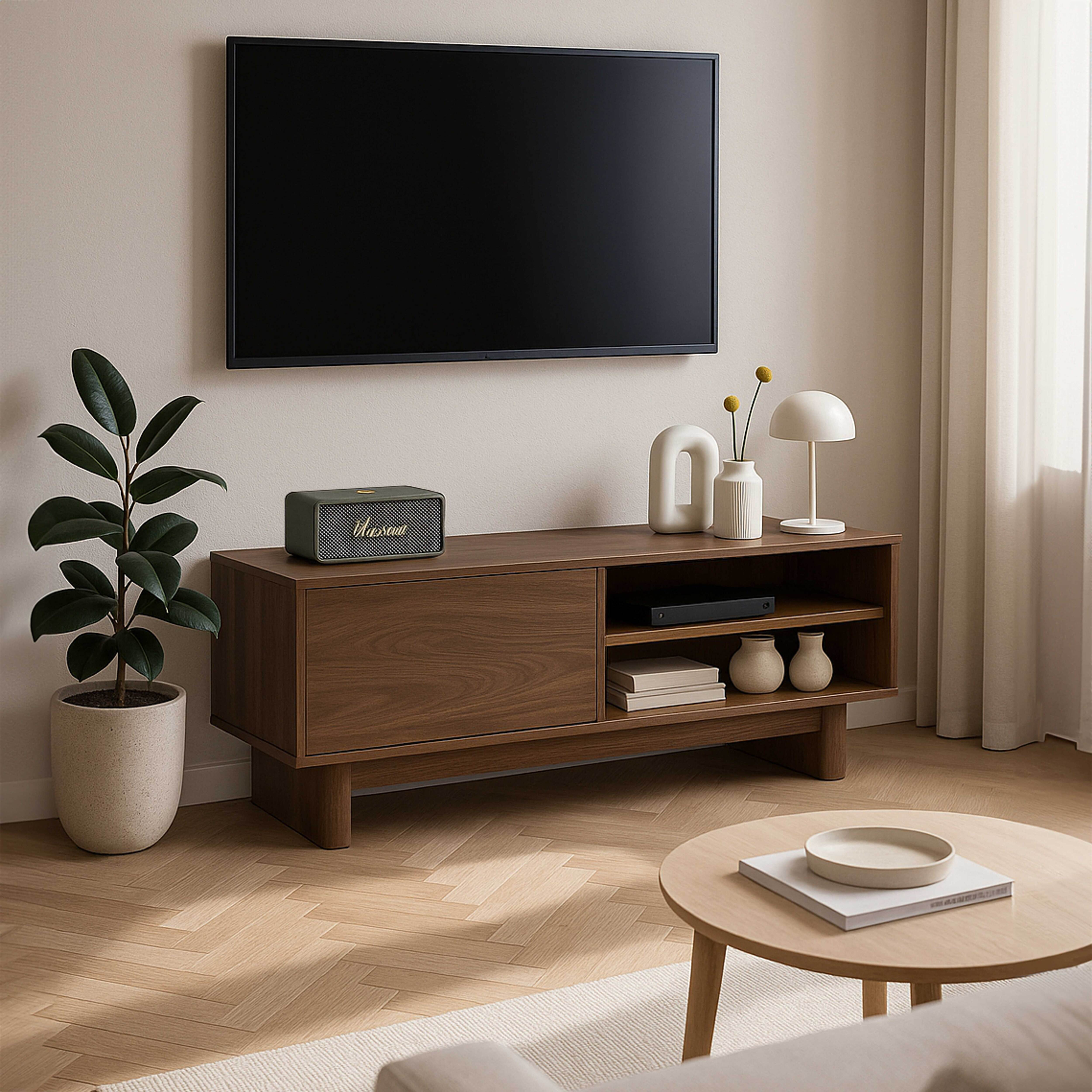 Ein Wohnzimmer mit Fernseher, Holzschrank, Pflanze, Lampe und rundem Couchtisch.
